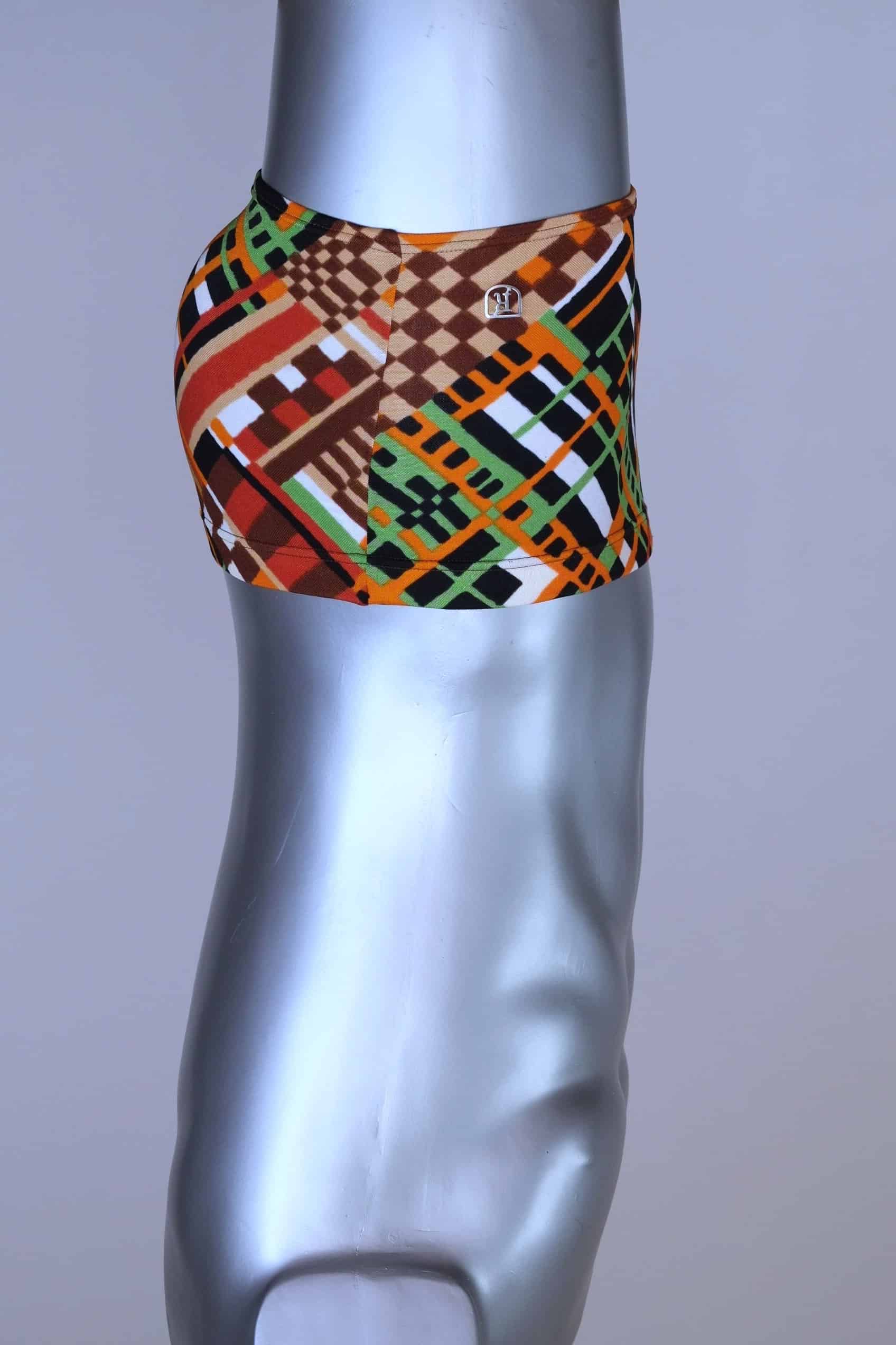 Side view of vintage 70s Ribana swim trunks in a geometric print with warm tones of orange, brown, green, and black, modeled on a silver mannequin.