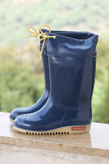 Navy ROMIKA Bobby Rain Boots on a wet ledge with trees background