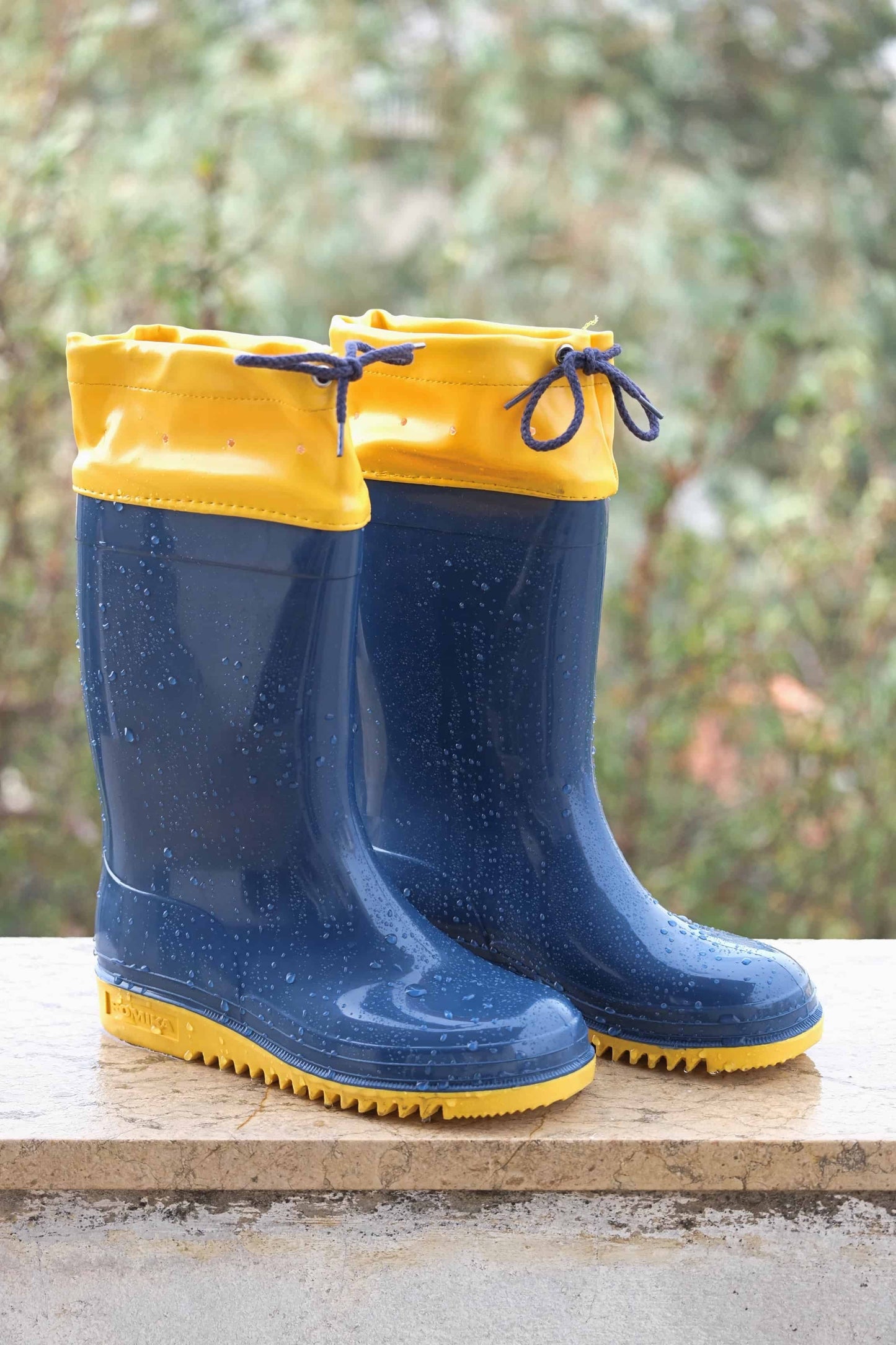 Navy and yellow ROMIKA Bobby Rain Boots on a ledge in the rain