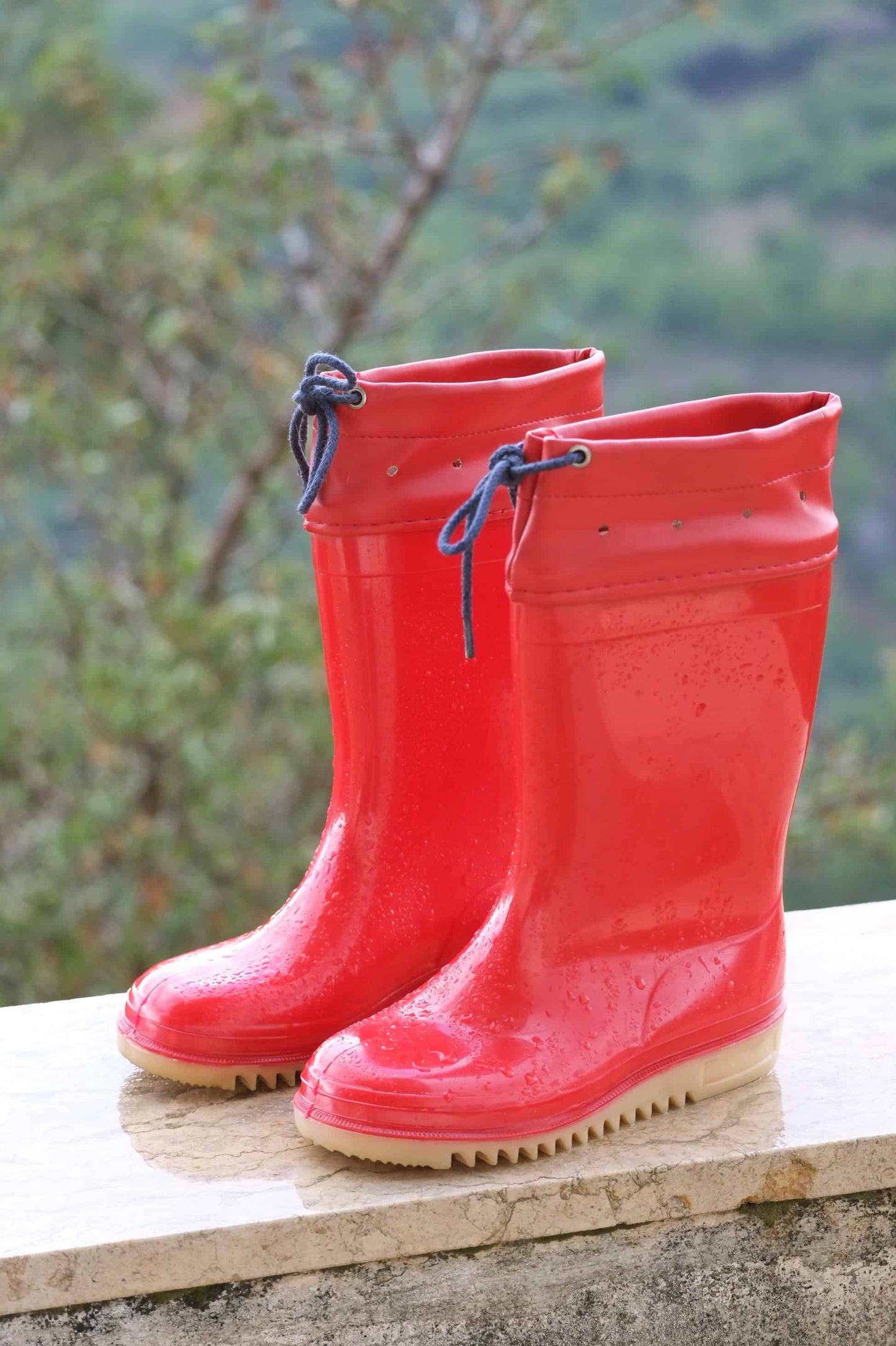 Red ROMIKA Bobby Rain Boots on a ledge and covered in rain drops