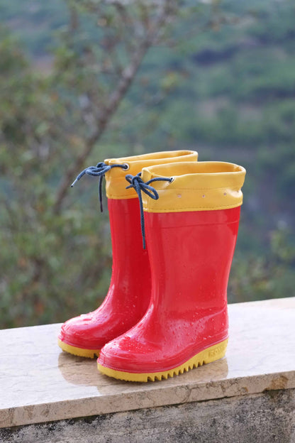 Red and yellow ROMIKA Bobby Rain Boots on a ledge with forest background