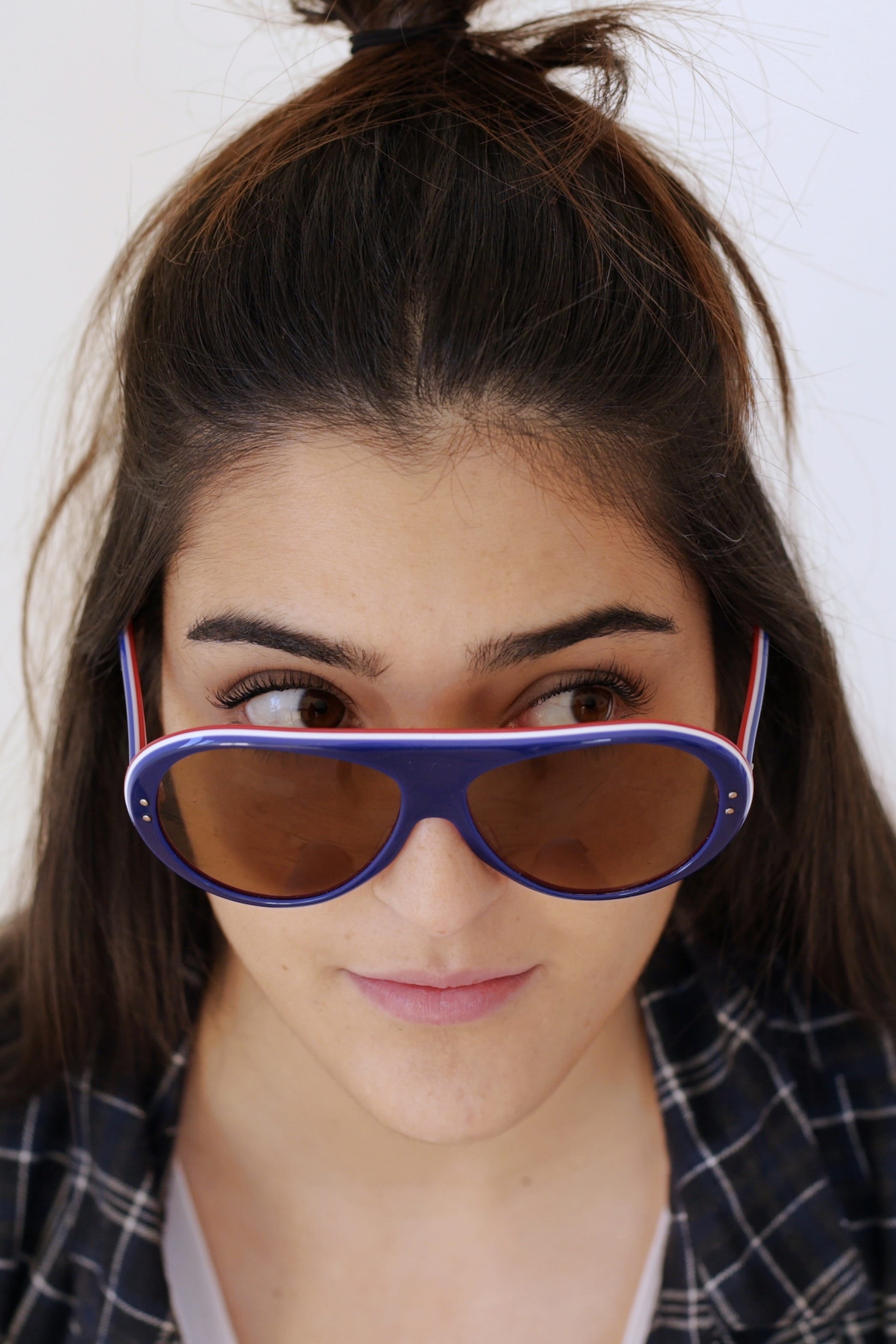 Woman wearing navy blue vintage SKILOOK 1970s tricolor ski sunglasses with brown lenses pulled slightly down her nose, showing the white-striped top frame rim and shield bridge design.