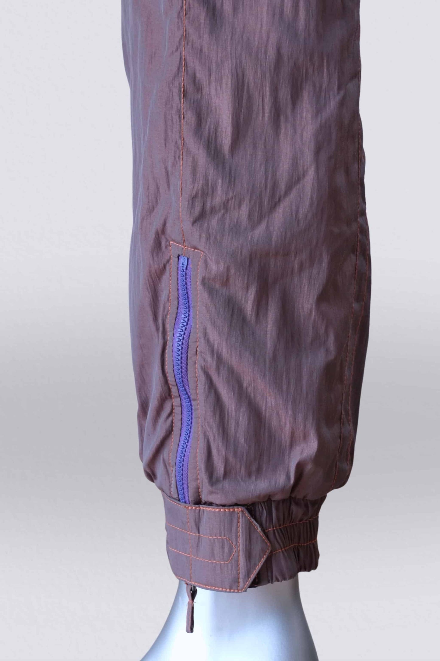 Detailed view of a brown 90s ski suit ankle featuring a purple zipper, elastic cuff, and a brown strap with orange stitching.