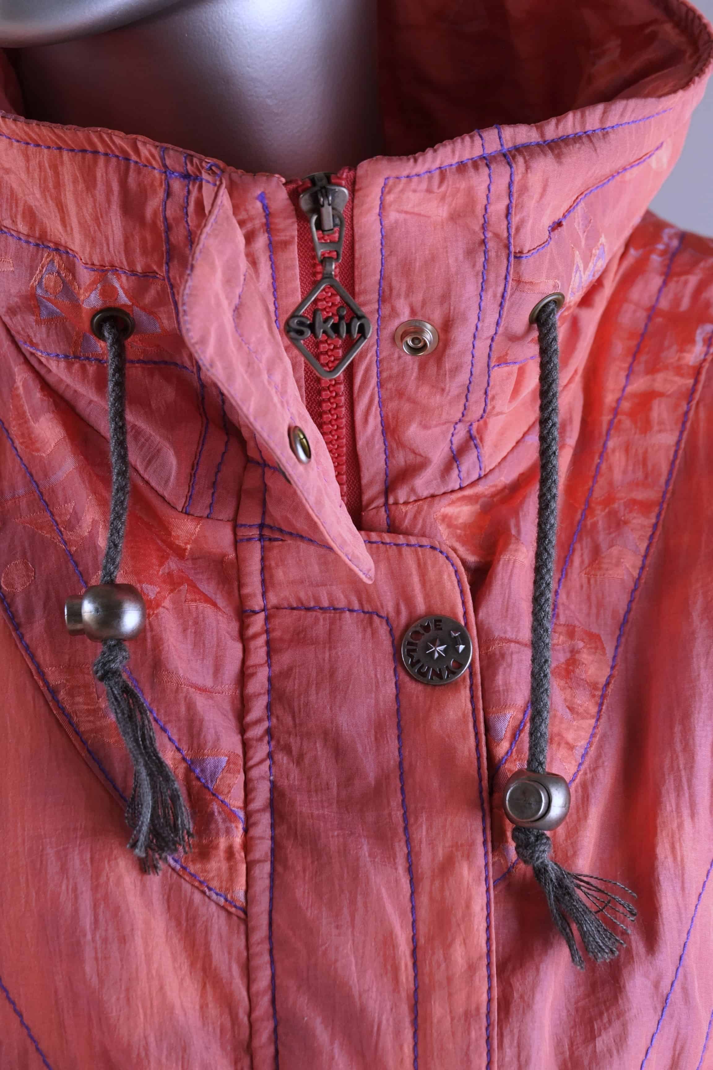 Detailed view of a coral 90s ski suit collar, showing a zipper, snap closures, drawstrings, and a 'Skin' brand zipper pull.