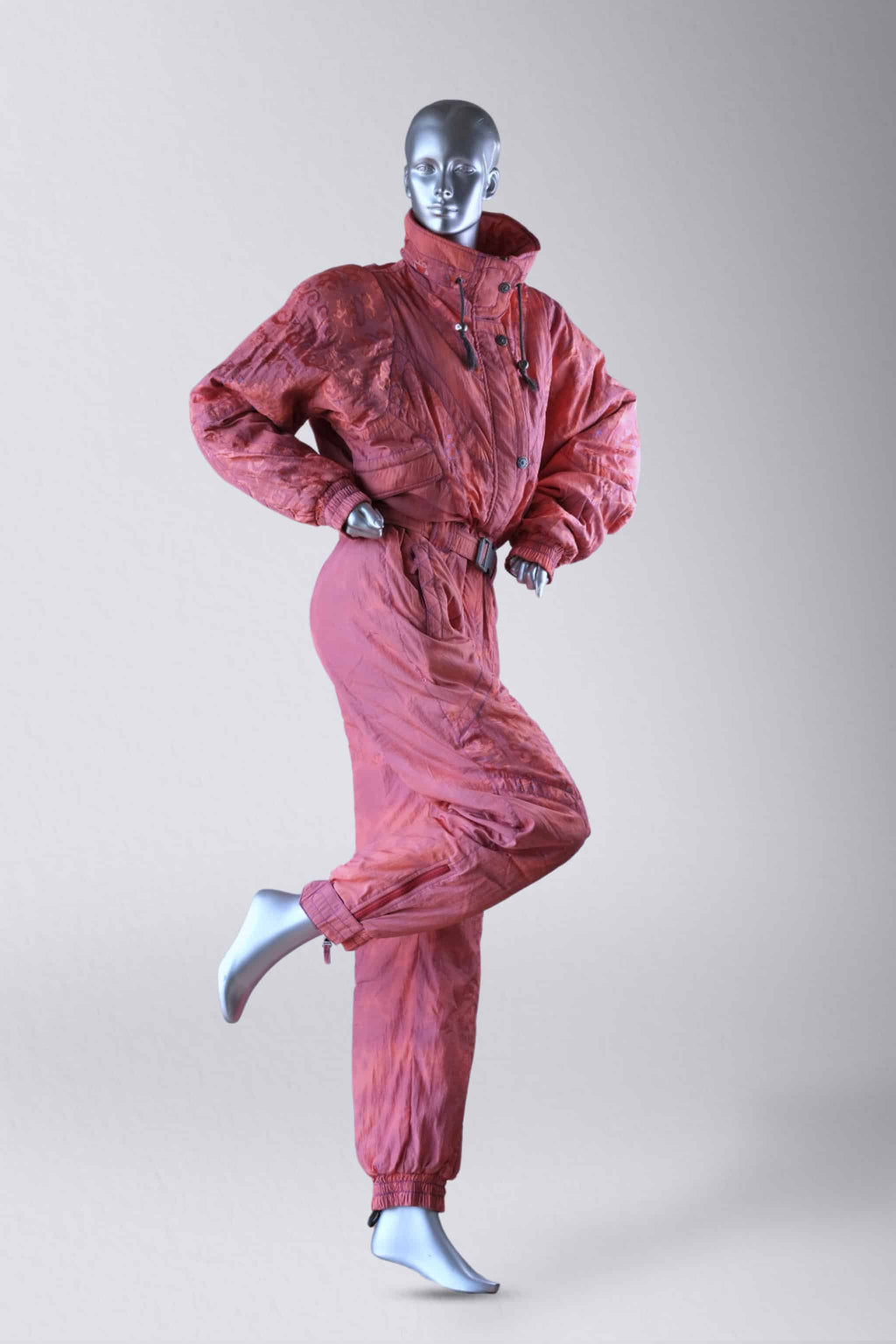 A full body shot of coral vintage 90s ski suit, shown on a mannequin with one leg raised.