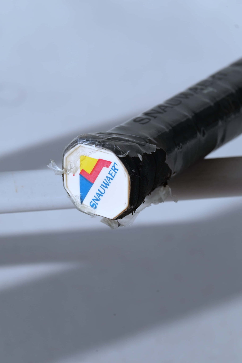 Close-up view of the white Snauwaert logo butt cap on a variation featuring a black wrapped grip.