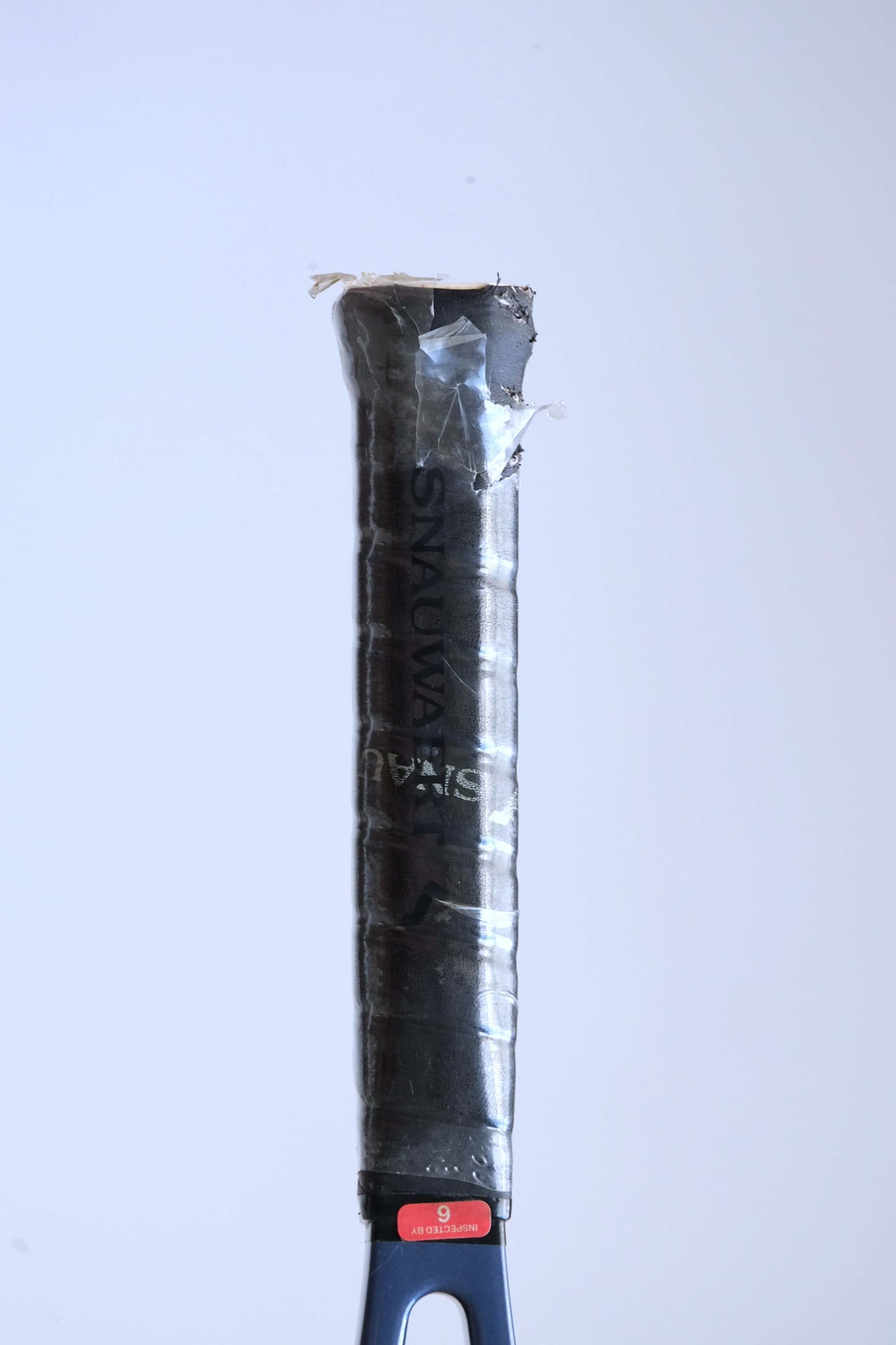 Detail shot of the racquet handle variation wrapped in a black synthetic Snauwaert grip with a red "Inspected By 6" sticker at the top.