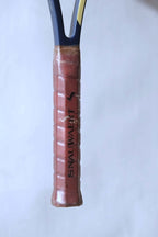 Detail shot of the racquet handle wrapped in its original brown leather Snauwaert-branded grip, encased in a clear protective plastic seal.