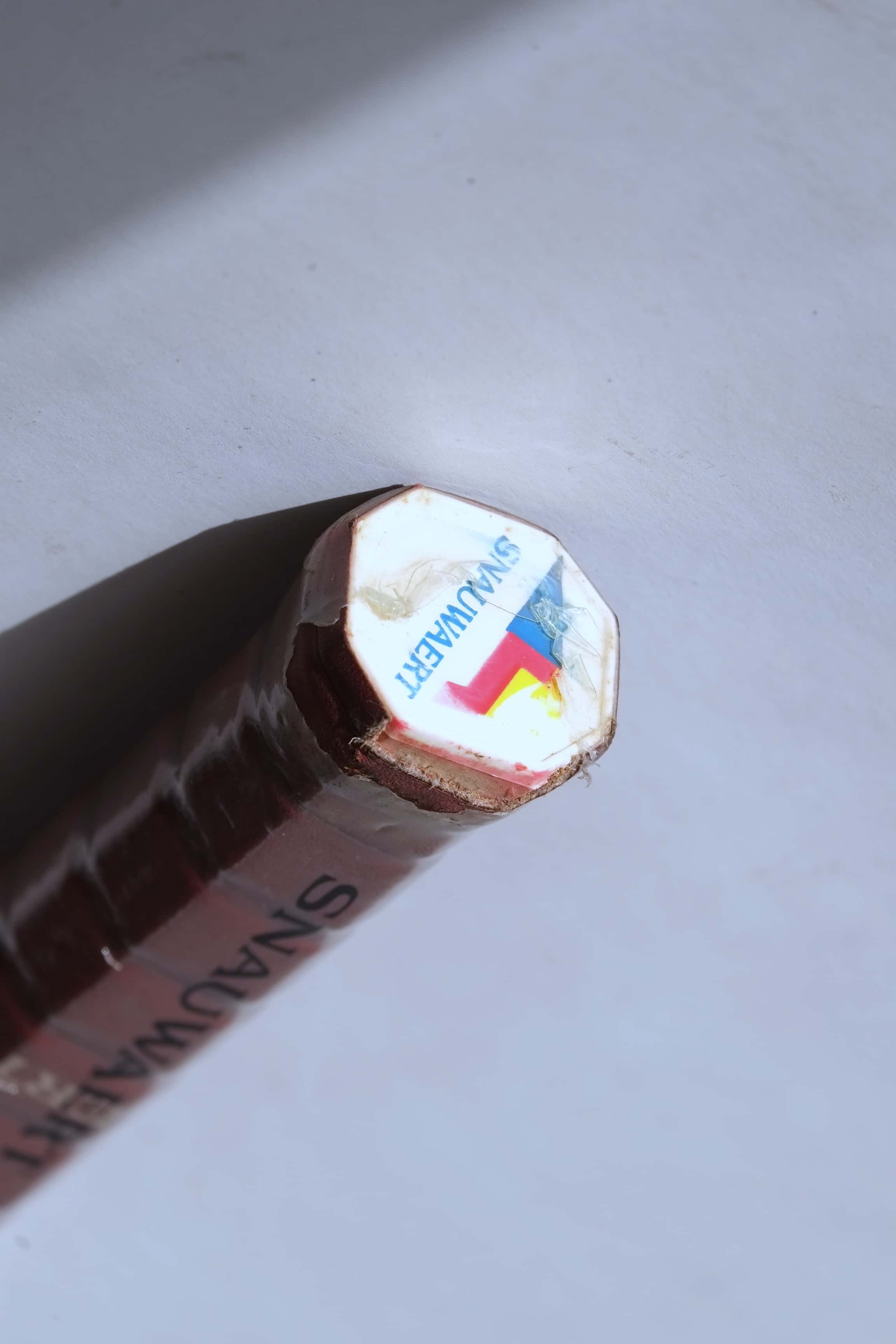 Angled close-up of the white racquet butt cap featuring the colorful Snauwaert geometric logo and name, sealed in original plastic film over a brown leather grip.