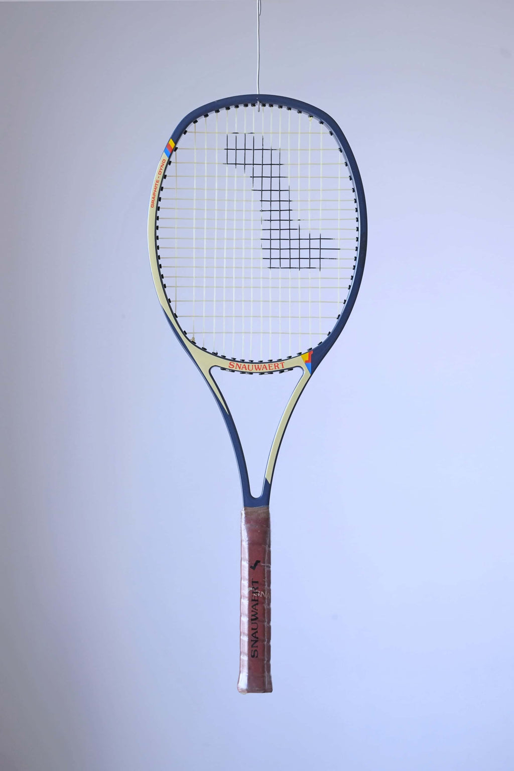 Studio full front shot of a strung early 80s Snauwaert Graphite Dyno tennis racquet with a brown leather grip, showing its signature Angled-Arc frame design.