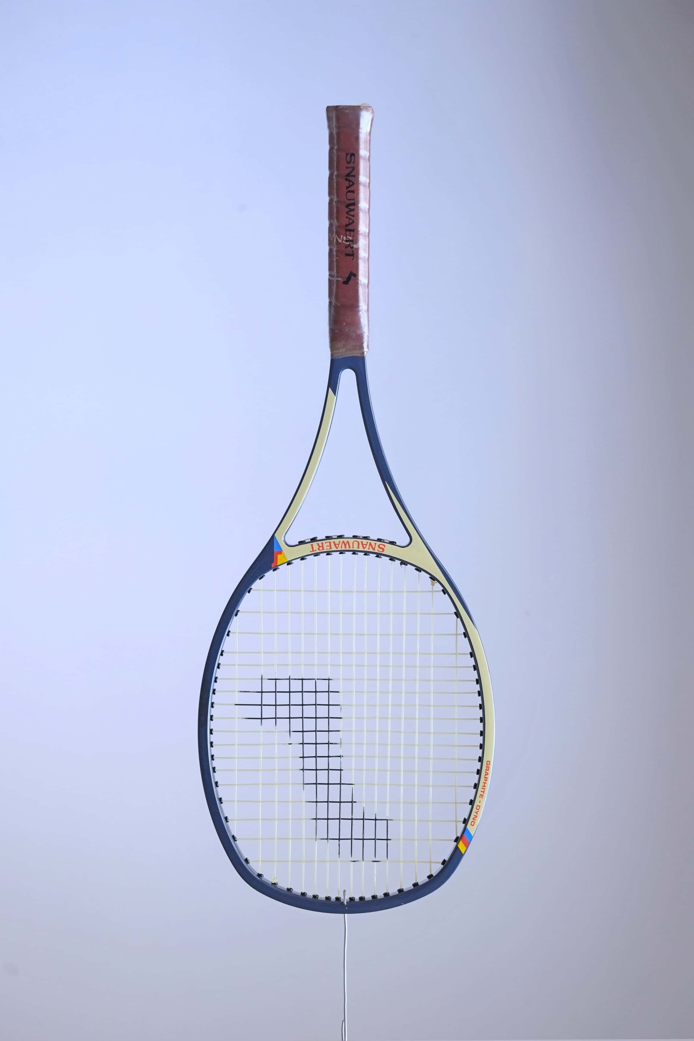 Studio full front shot of a strung early 80s Snauwaert Graphite Dyno tennis racquet with a brown leather grip, showing its signature Angled-Arc frame design.