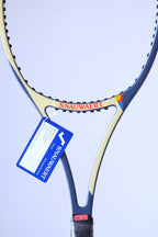 Close-up of the racquet throat area showcasing the red "SNAUWAERT" branding on a cream background, a blue paper warranty tag, and the red inspection sticker.