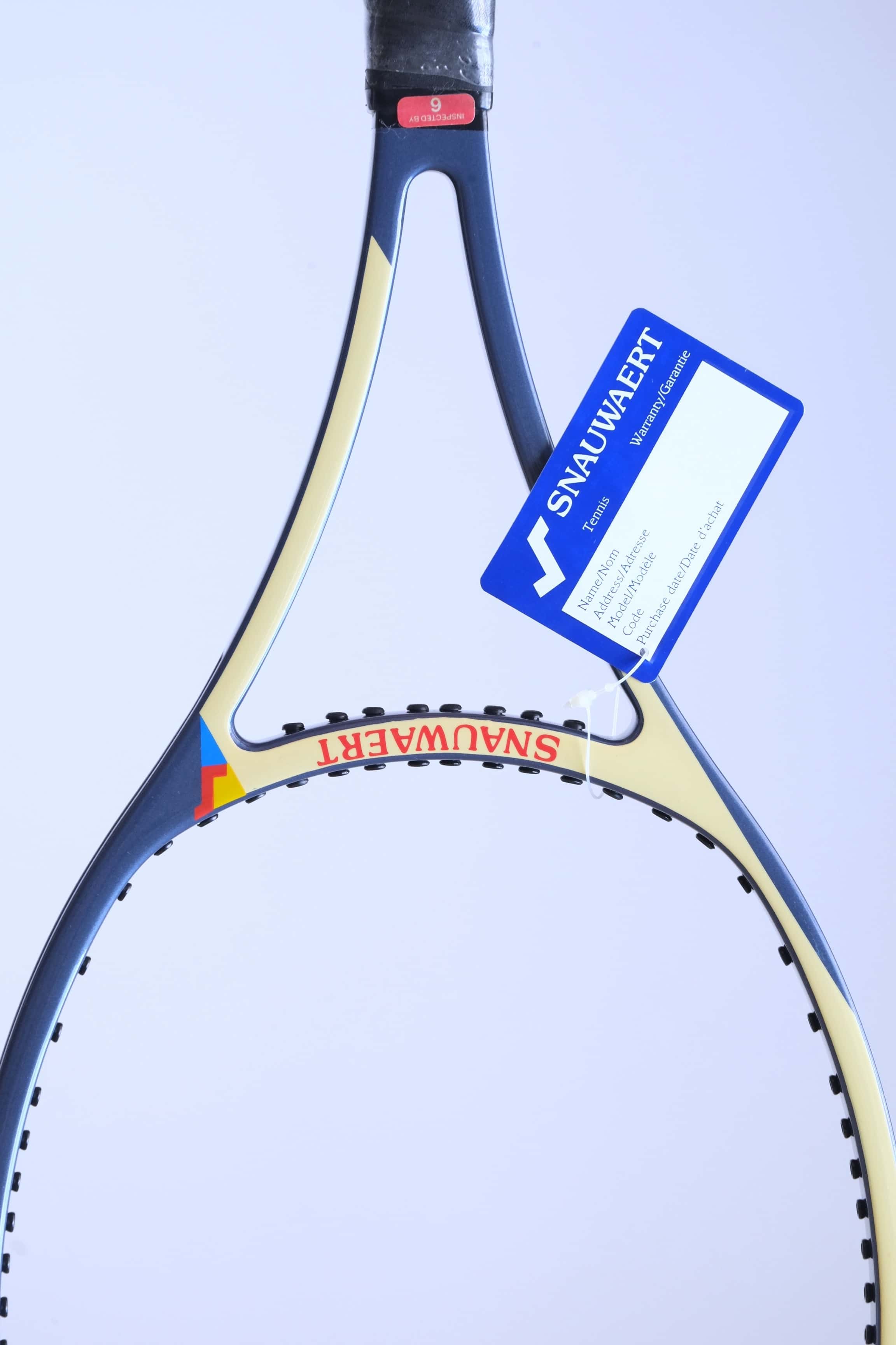 Close-up of the racquet throat area showcasing the red "SNAUWAERT" branding on a cream background, a blue paper warranty tag, and the red inspection sticker.