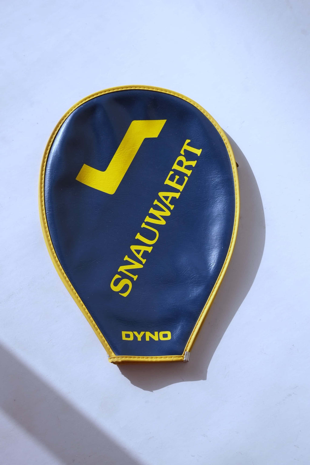 Top-down view of the full navy blue vinyl racquet cover featuring a large yellow Snauwaert logo and name, framed by a yellow stitched trim.