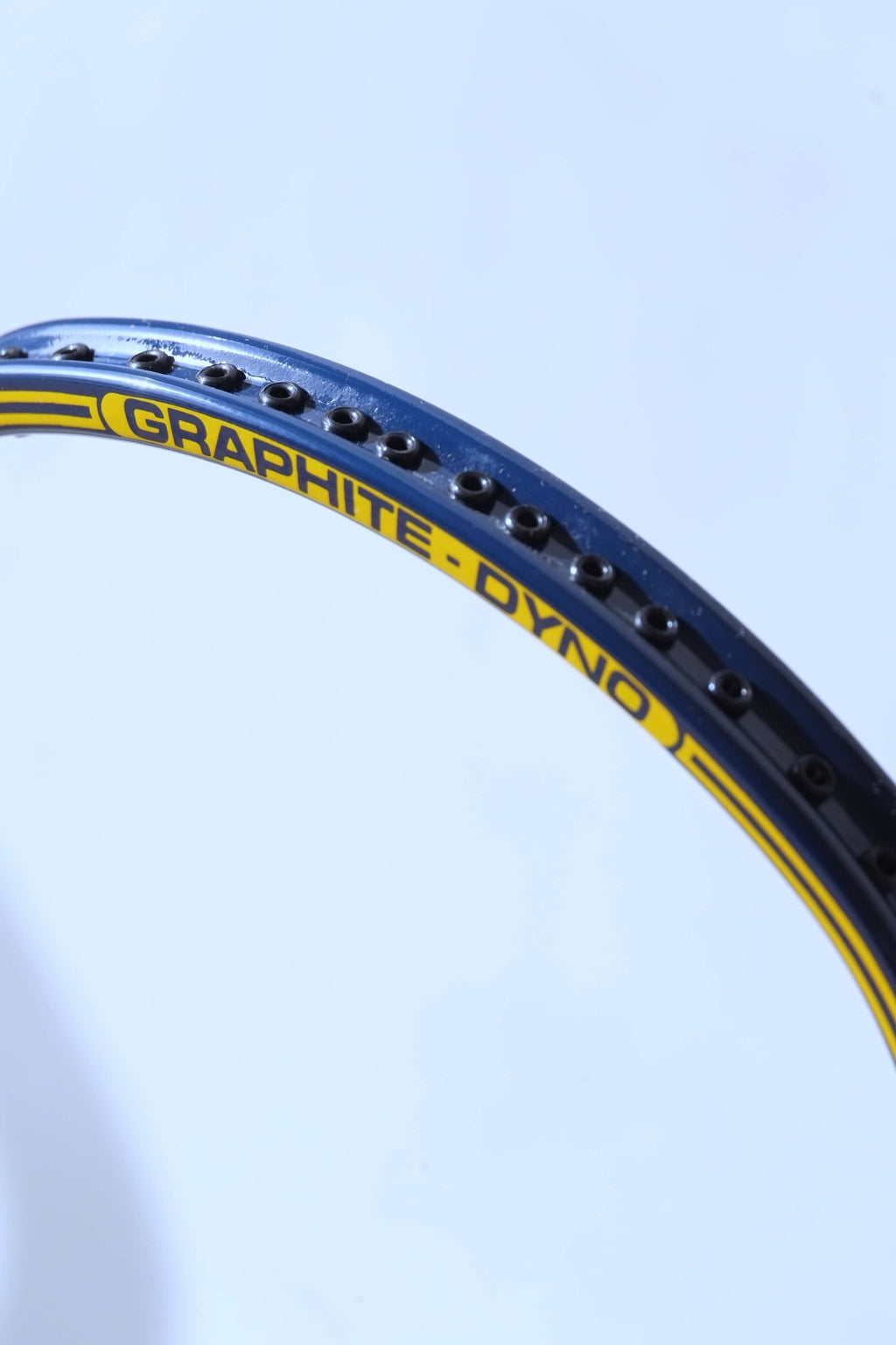 Macro side profile shot of the blue racquet frame highlighting a row of empty black string grommets along the outer channel.