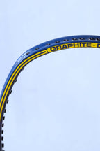 Angled close-up of the upper racquet hoop showcasing the yellow "GRAPHITE - DYNO" model name text printed on a yellow accent stripe against the blue frame.