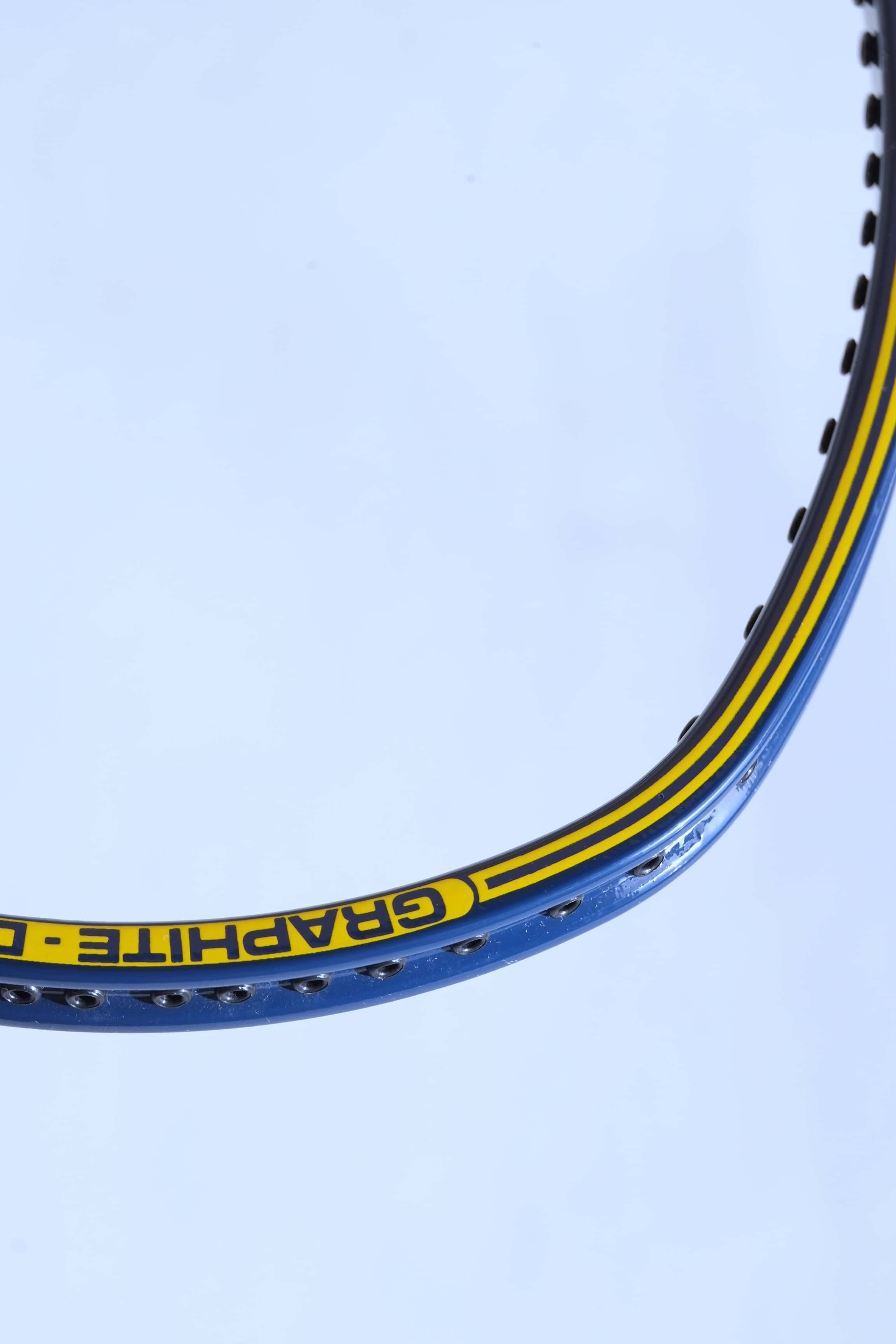 Angled close-up of the upper racquet hoop showcasing the yellow "GRAPHITE - DYNO" model name text printed on a yellow accent stripe against the blue frame.