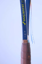 Close-up of the racquet handle's upper shaft featuring the yellow Snauwaert logo, "MADE IN BELGIUM" text, and printed grip/weight specifications above the leather wrap.