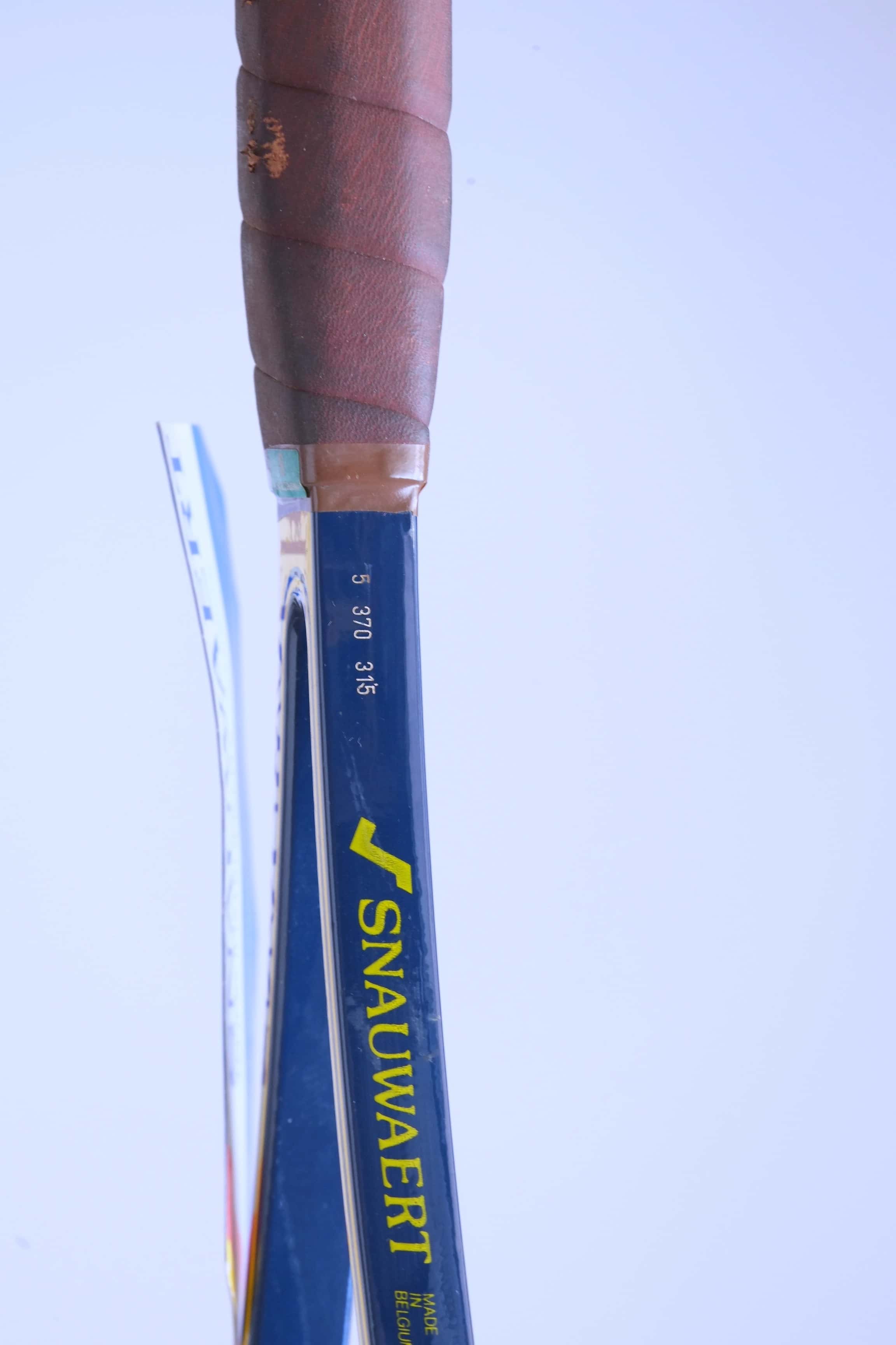 Close-up of the racquet handle's upper shaft featuring the yellow Snauwaert logo, "MADE IN BELGIUM" text, and printed grip/weight specifications above the leather wrap.