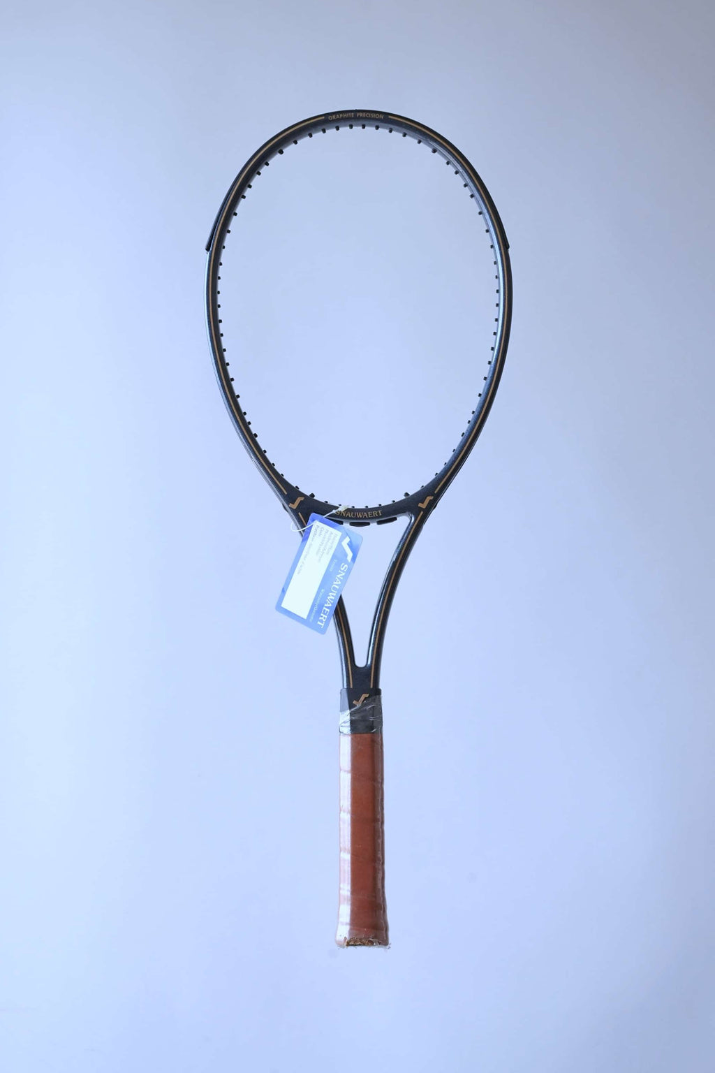 Full front view of a vintage unstrung Snauwaert Graphite Precision tennis racquet with a brown leather grip and a blue warranty tag attached.