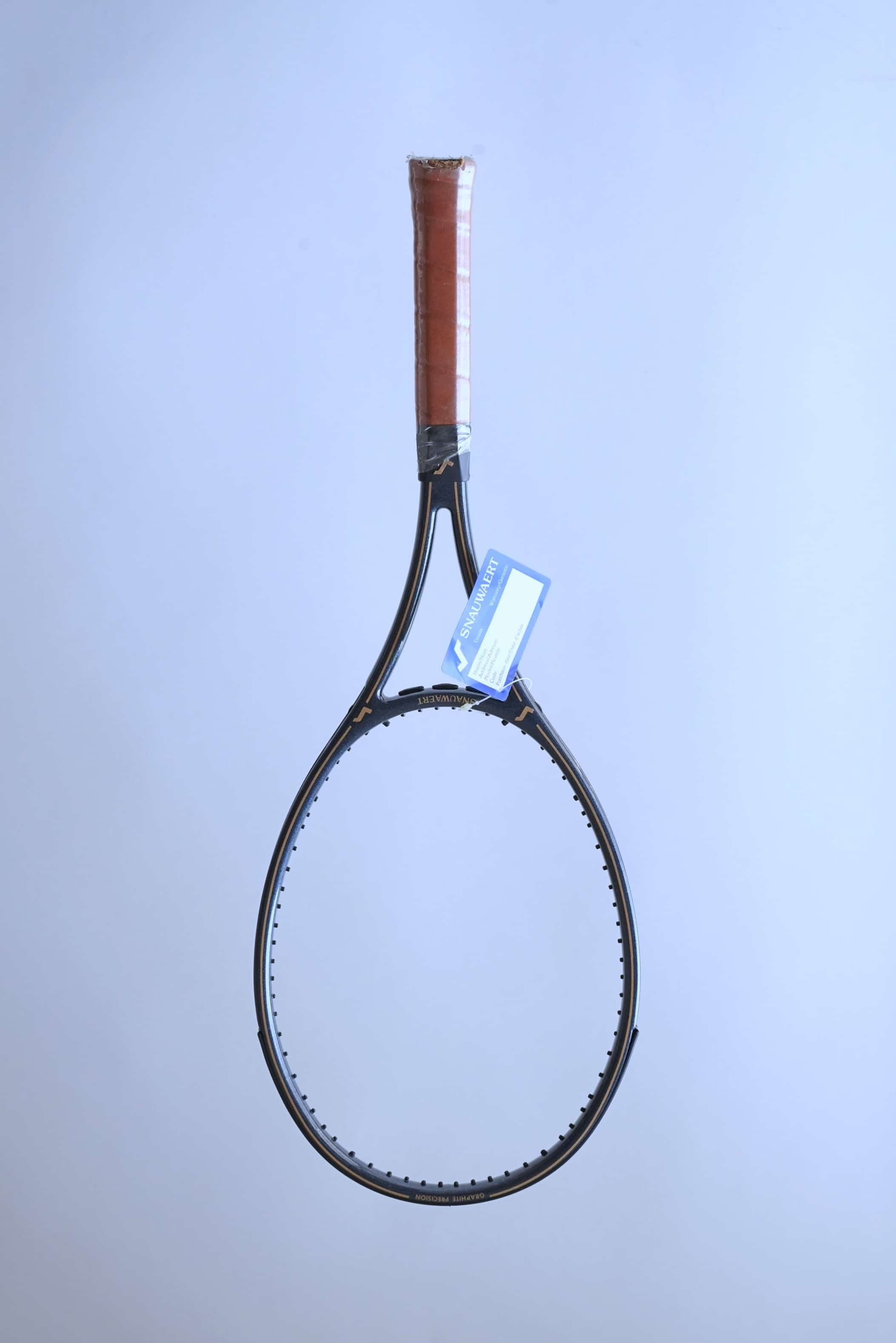Full front view of a vintage unstrung Snauwaert Graphite Precision tennis racquet with a brown leather grip and a blue warranty tag attached.