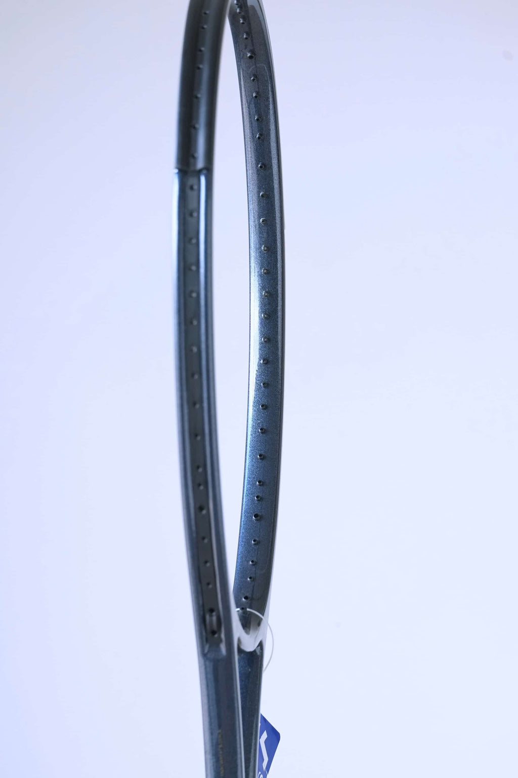Side profile of the empty racquet head, highlighting the dark grey speckled graphite finish and string grommet holes.