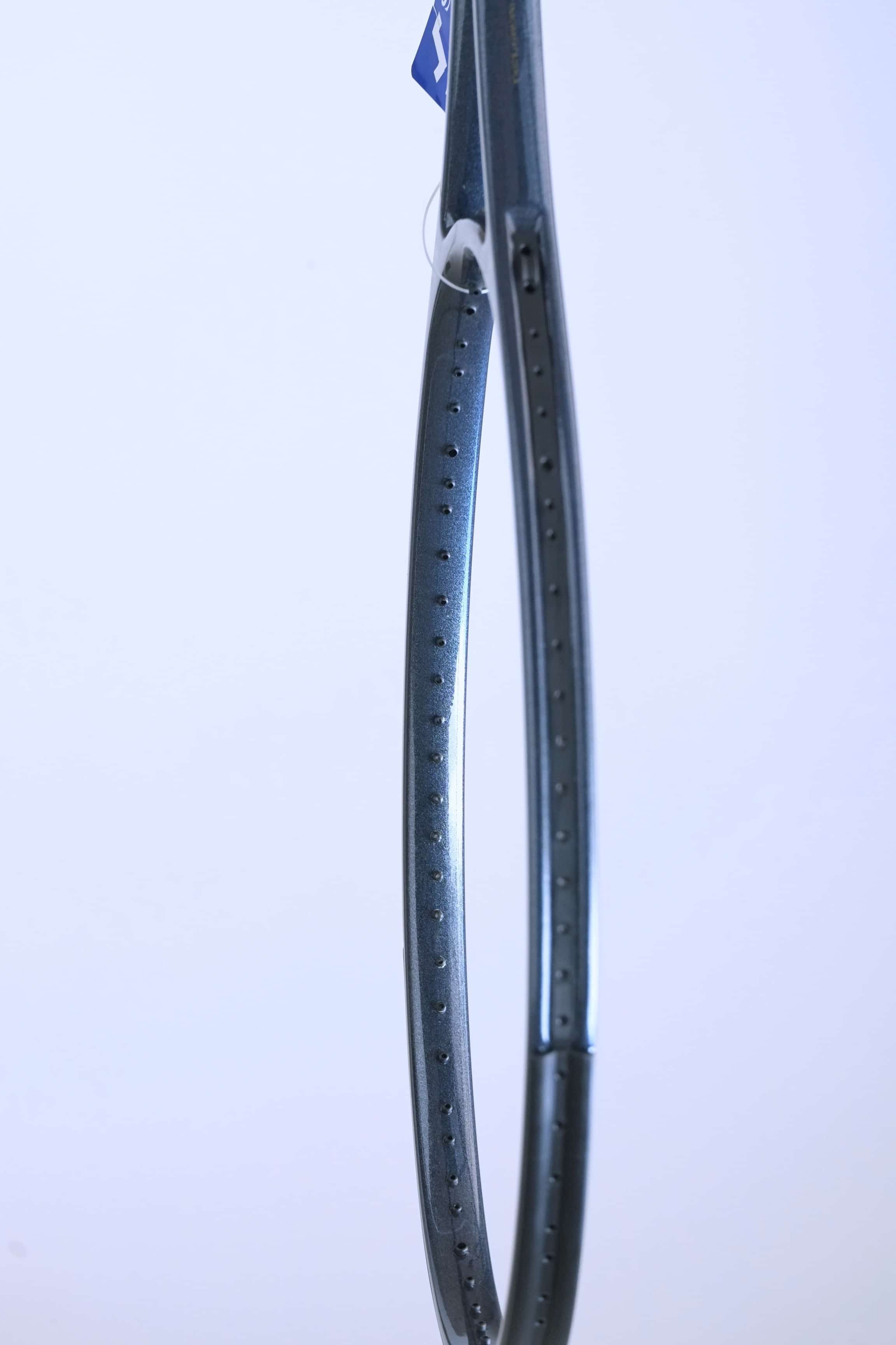Side profile of the empty racquet head, highlighting the dark grey speckled graphite finish and string grommet holes.