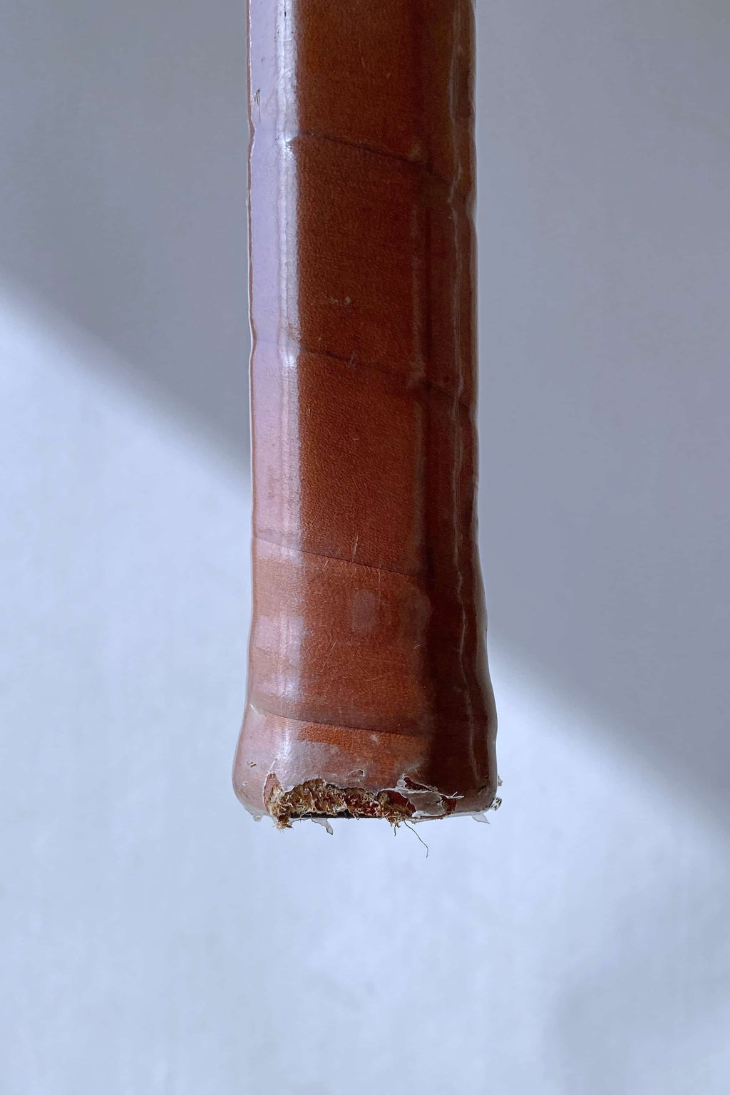 Detailed view of the bottom of the racquet handle, showing the worn leather and clear protective wrap at the base.