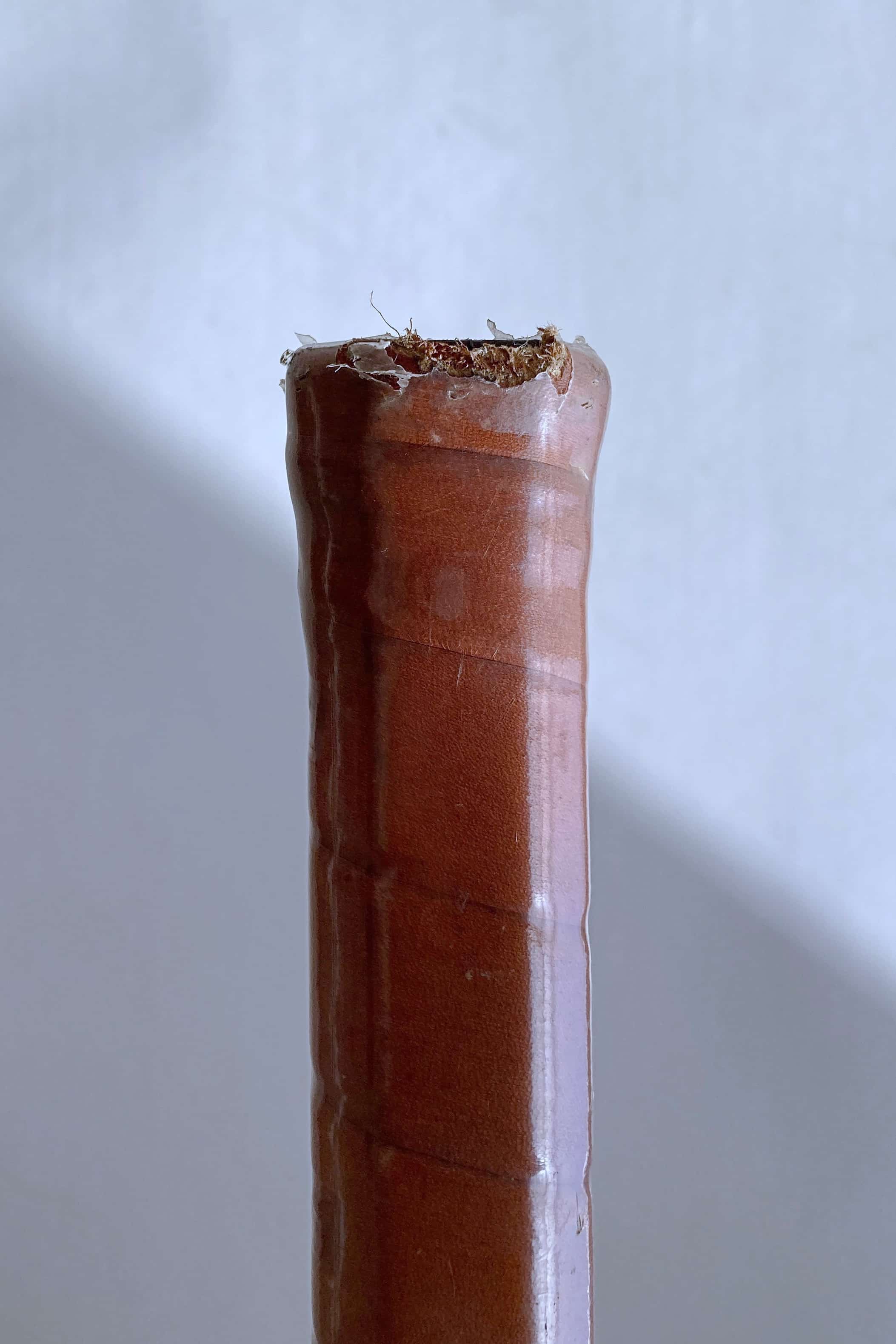 Detailed view of the bottom of the racquet handle, showing the worn leather and clear protective wrap at the base.
