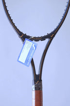 Vertical close-up of the racquet throat with gold pinstriping and a blue Snauwaert warranty card hanging by a white string.