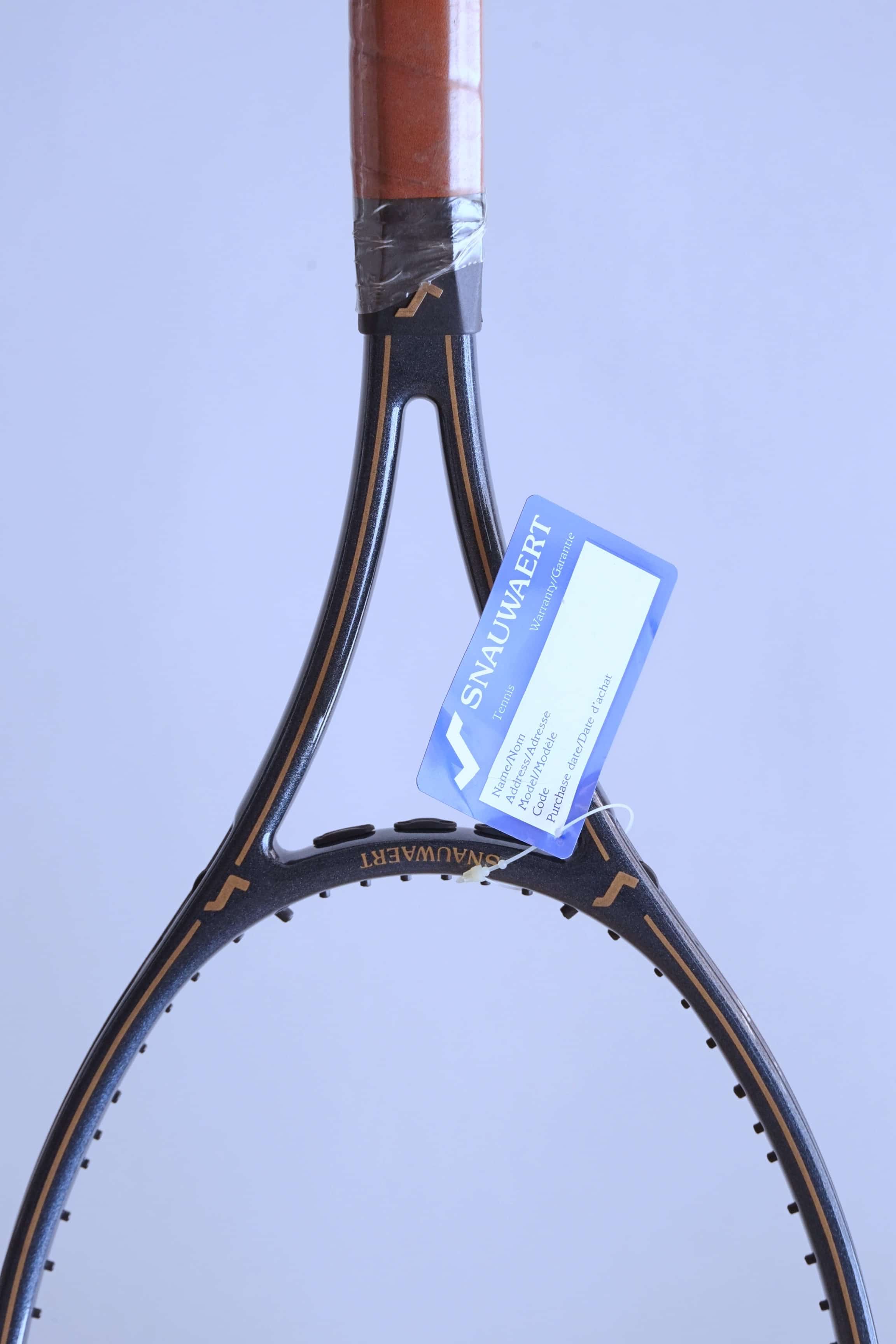 Vertical close-up of the racquet throat with gold pinstriping and a blue Snauwaert warranty card hanging by a white string.