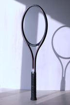 An unstrung vintage Snauwaert Graphite Pro tennis racquet stands vertically, casting a distinct shadow on a white background.