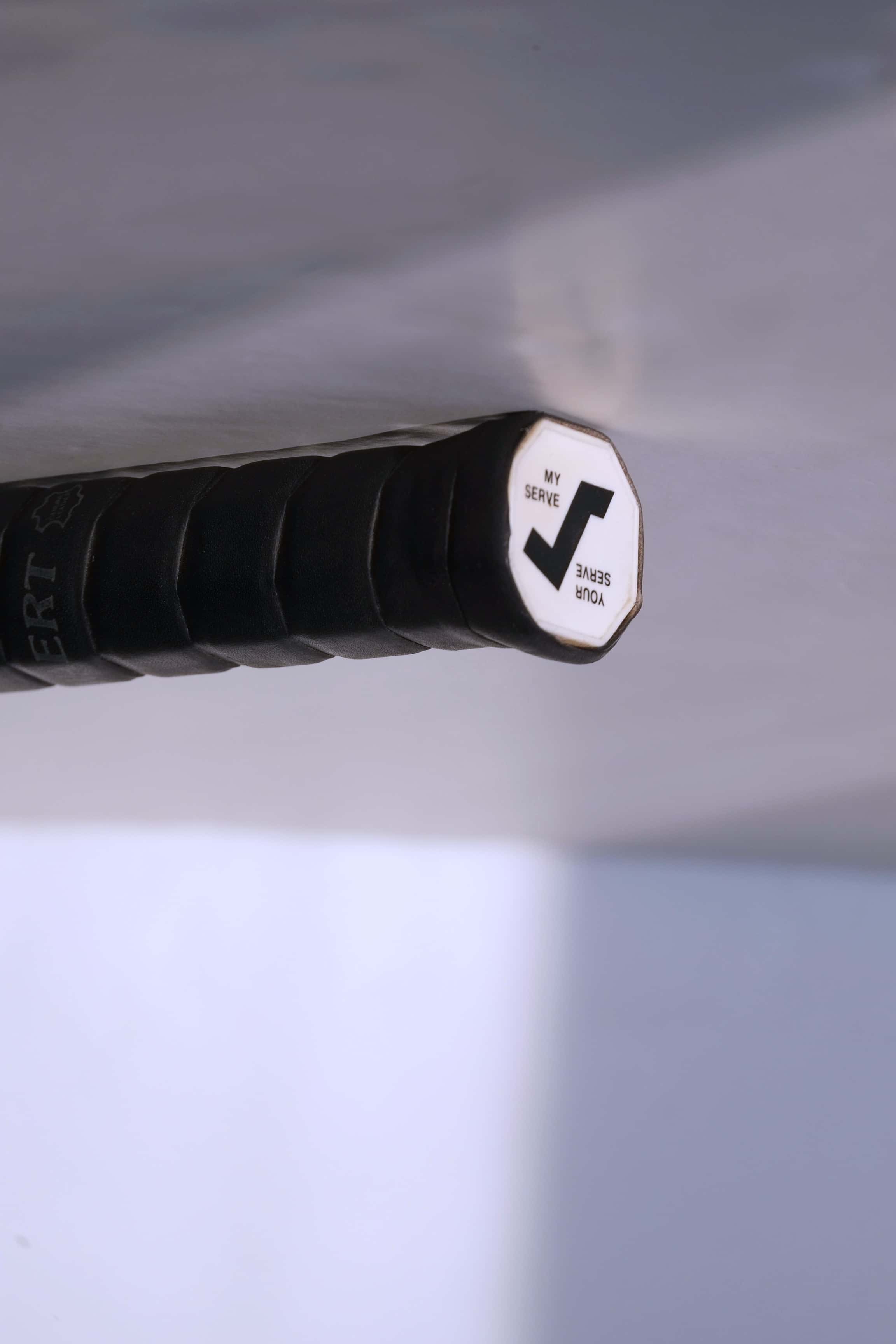 Close-up of the octagonal white butt cap featuring a black stylized "S" logo and the text "YOUR SERVE / MY SERVE".