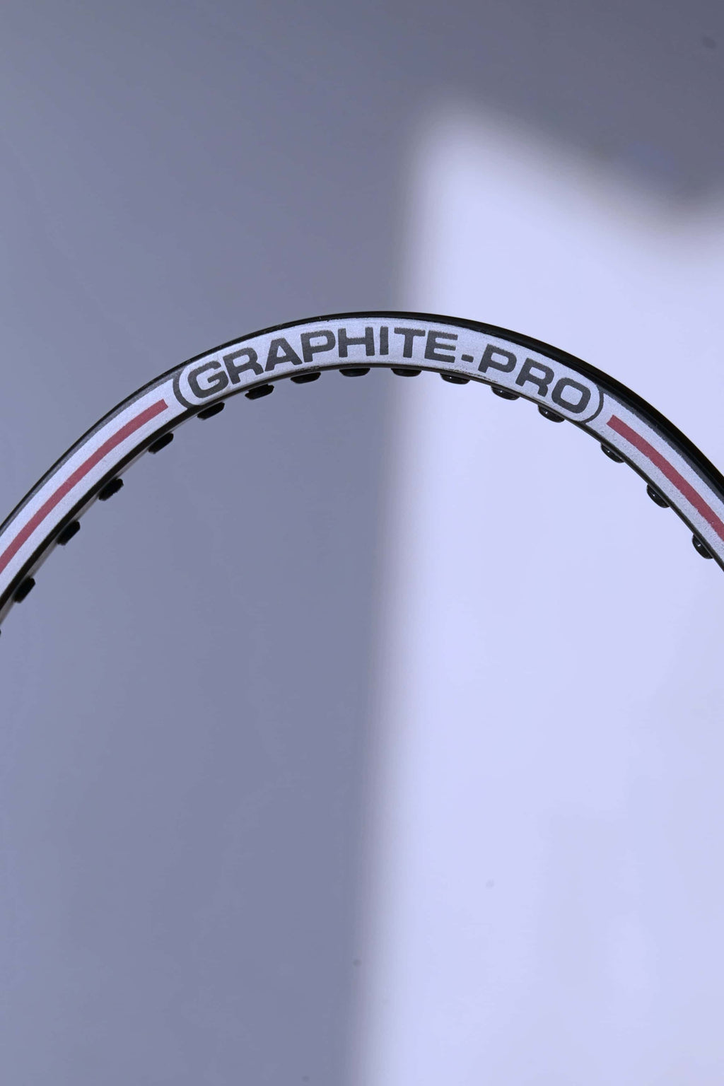Macro view of the top of the unstrung hoop showing the "GRAPHITE-PRO" branding and the white and red pinstripe detailing.