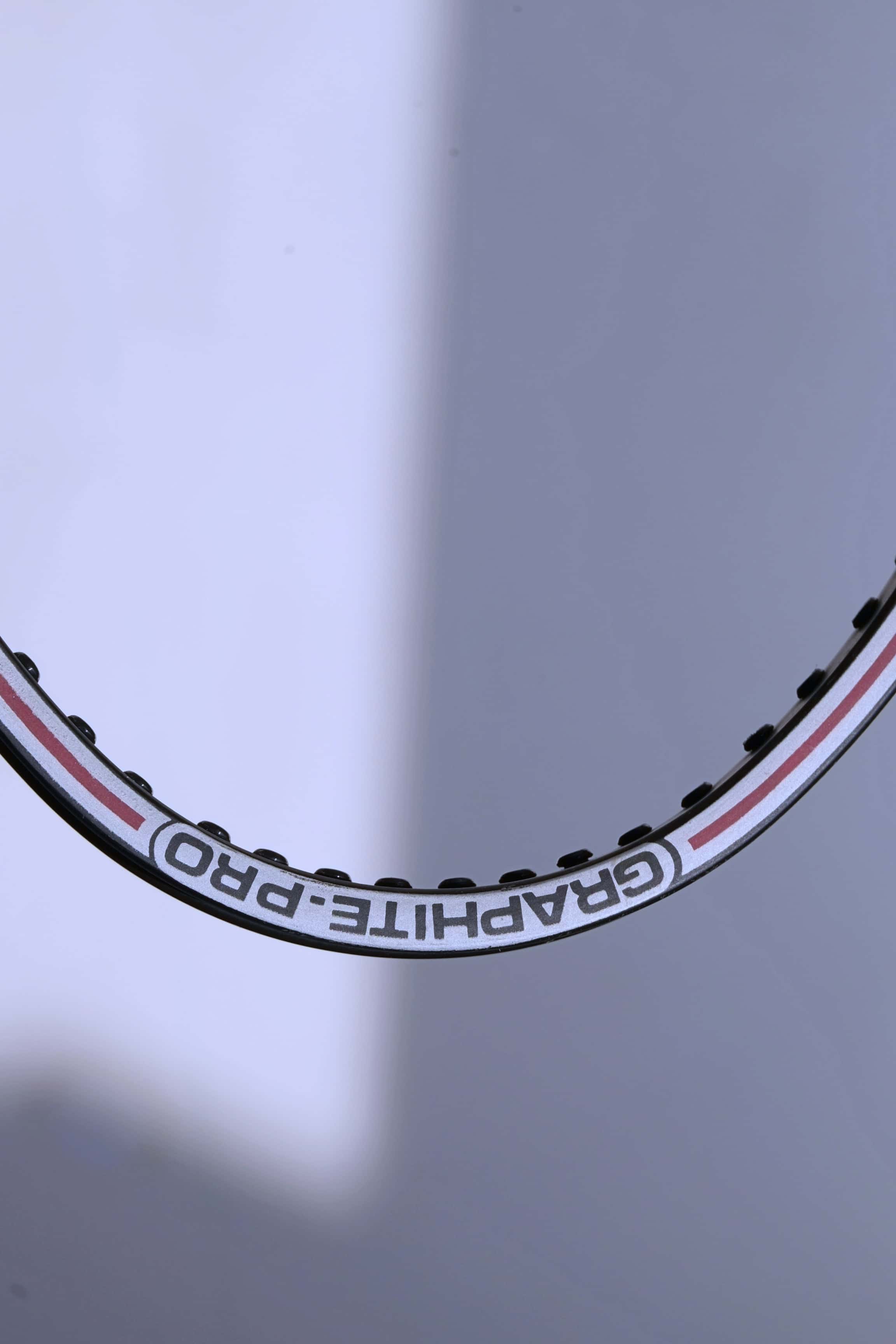 Macro view of the top of the unstrung hoop showing the "GRAPHITE-PRO" branding and the white and red pinstripe detailing.