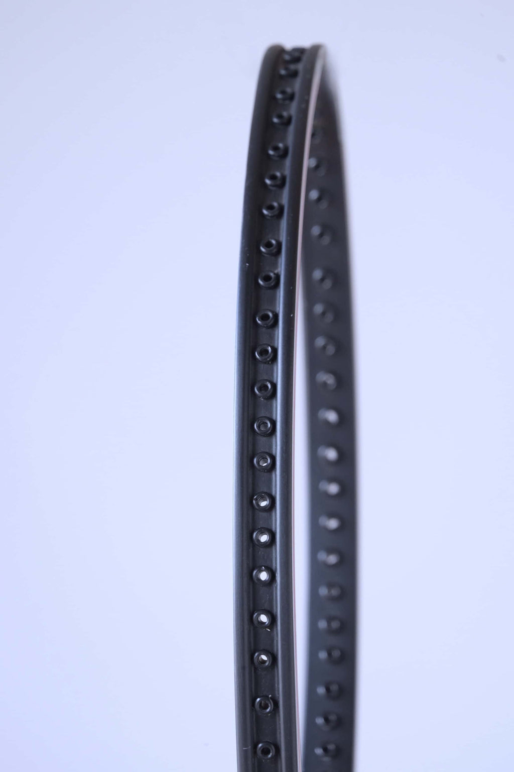 Profile view of the empty black racquet frame showing the precise row of grommet holes for stringing.
