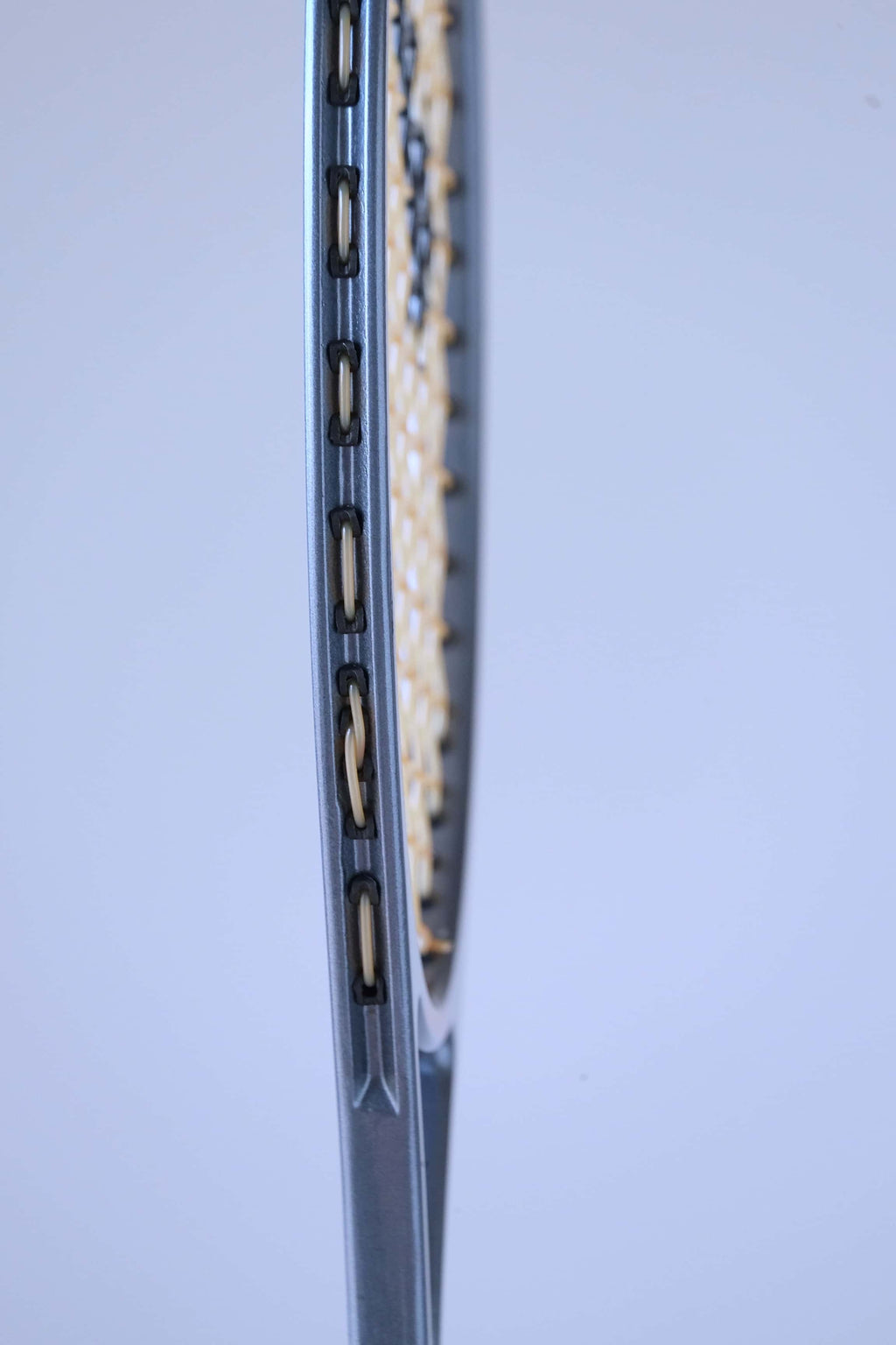Close-up view of the outer side of the frame showing the plastic string grommets of a vintage squash racket.