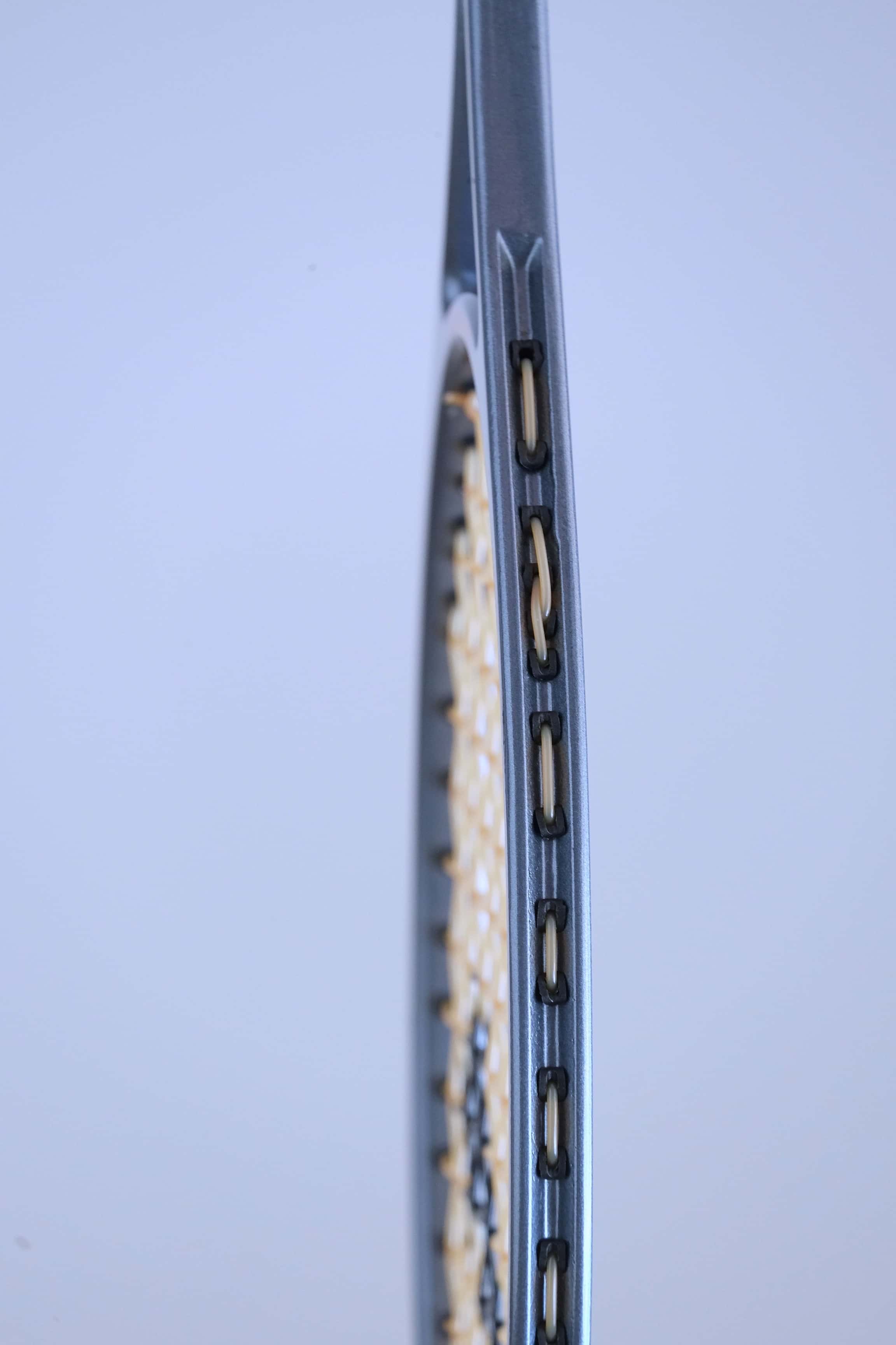 Close-up view of the outer side of the frame showing the plastic string grommets of a vintage squash racket.