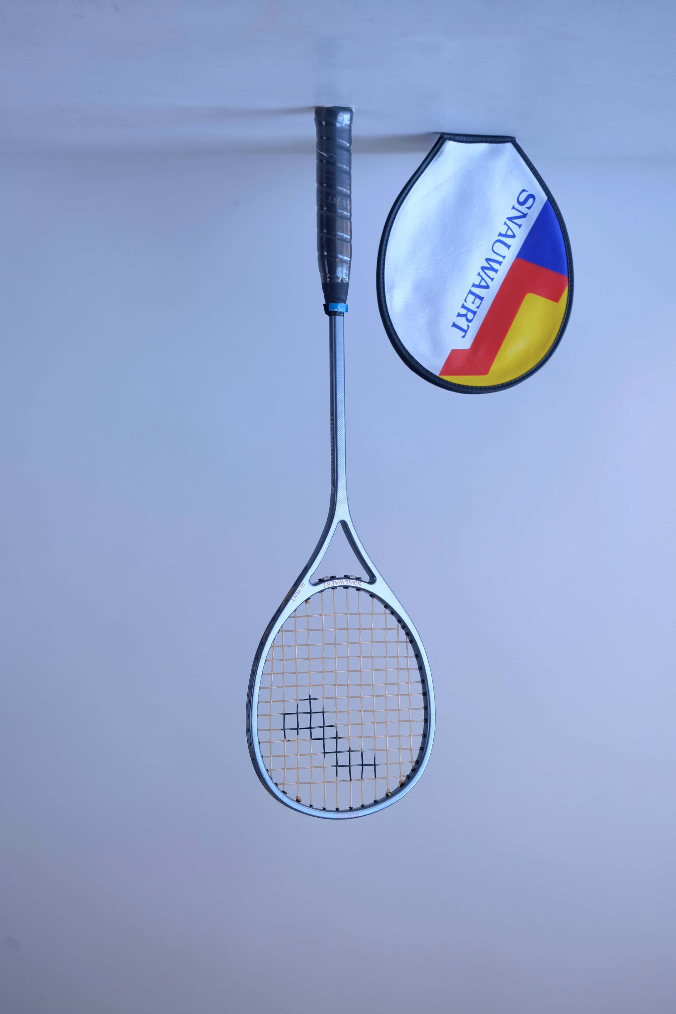 Full front view of a vintage strung Snauwaert Hi-Ten I squash racket standing against a plain background, next to its vinyl cover.