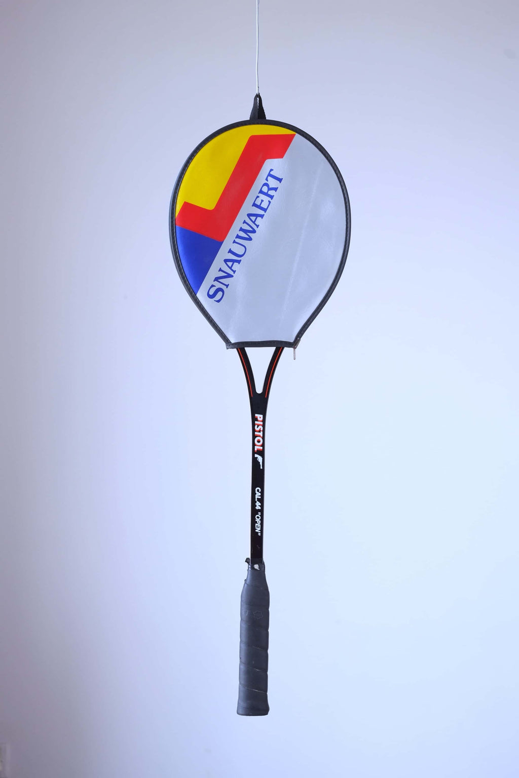 Vintage black Snauwaert Pistol squash racket hanging vertically inside a grey, yellow, and blue zippered vinyl cover.
