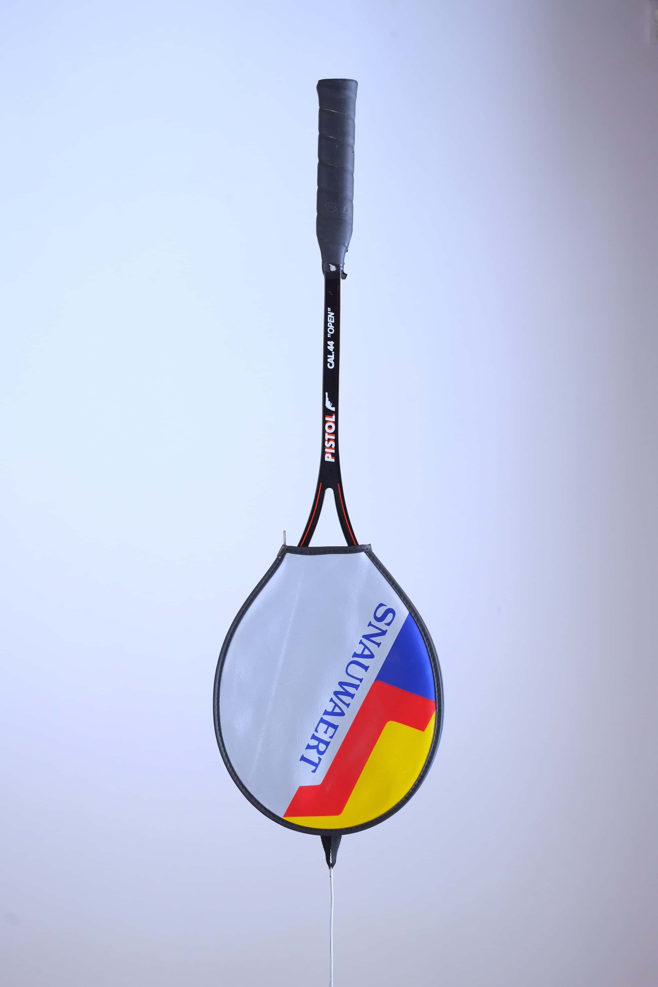 Vintage black Snauwaert Pistol squash racket hanging vertically inside a grey, yellow, and blue zippered vinyl cover.