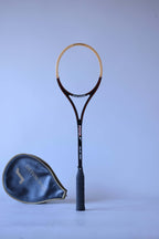 Vintage unstrung Snauwaert Pistol wood squash racket standing upright next to its matching black vinyl head cover.