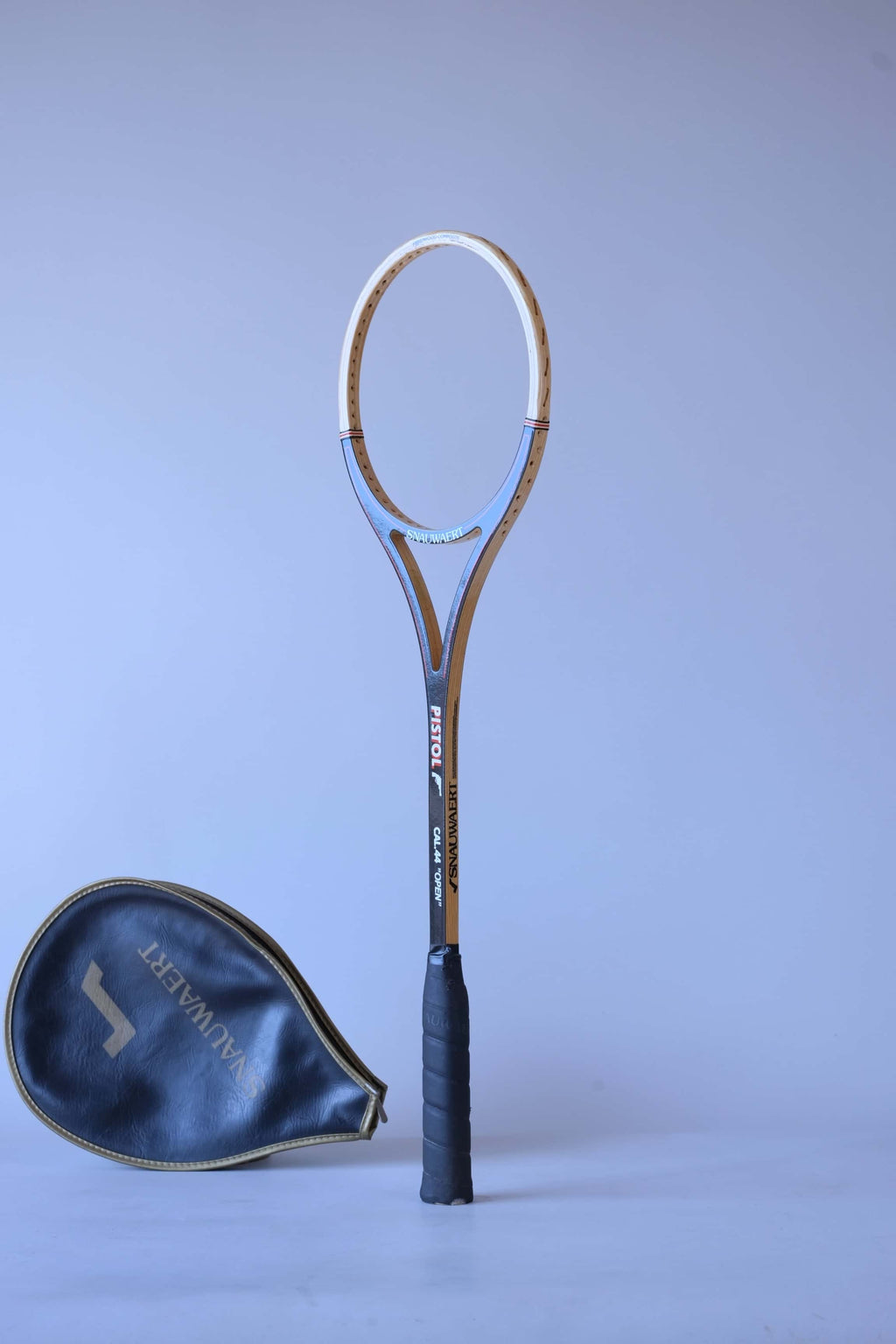 Vintage unstrung Snauwaert Pistol wood squash racket standing upright at an angle next to its matching black vinyl head cover.
