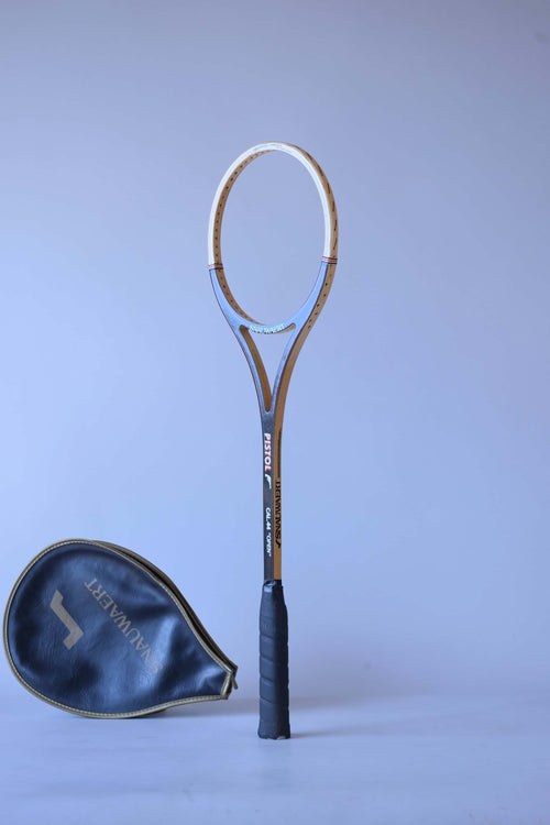 Vintage unstrung Snauwaert Pistol wood squash racket standing upright at an angle next to its matching black vinyl head cover.