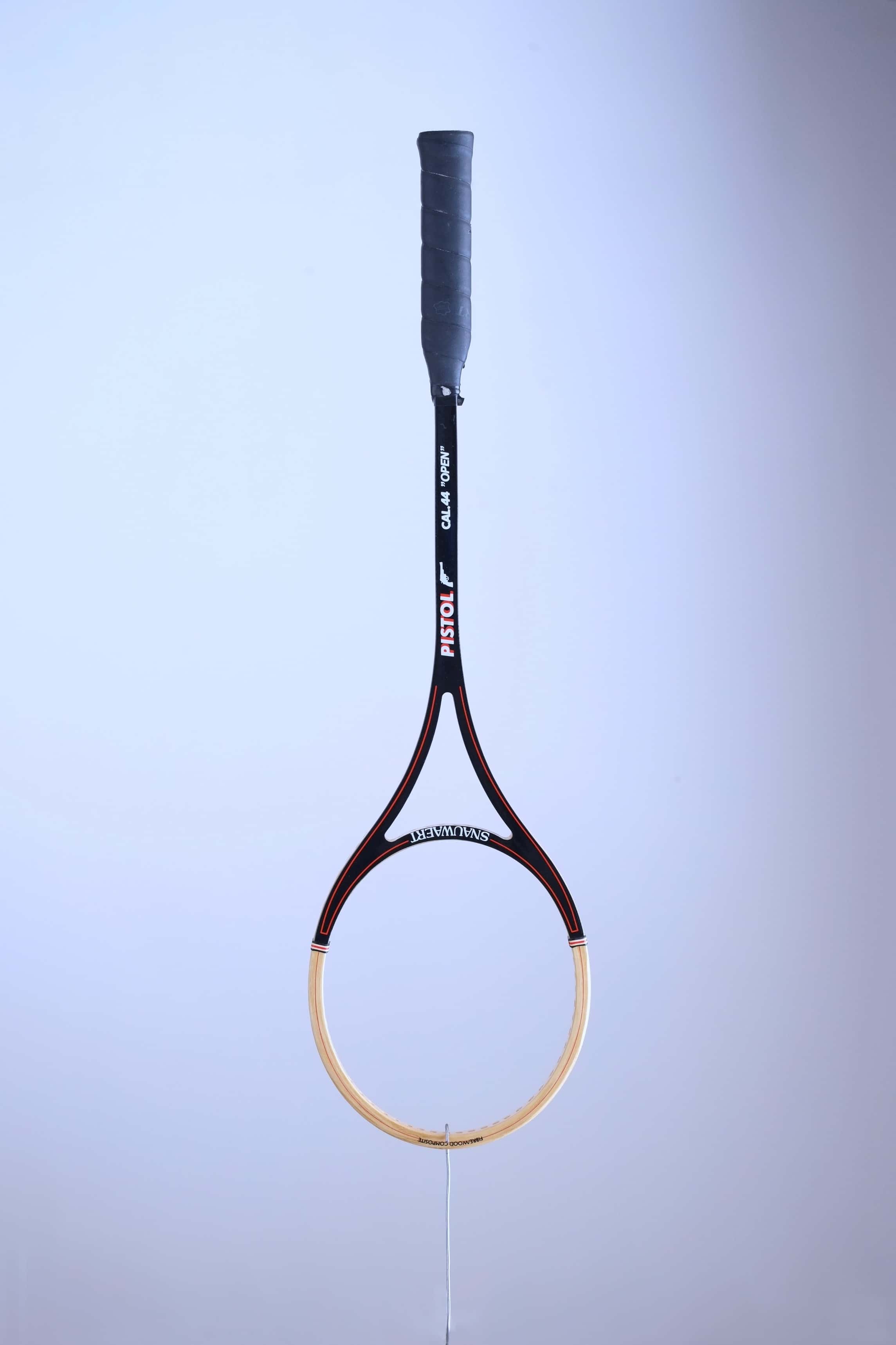Full front view of an unstrung vintage Snauwaert Pistol Cal 44 Open squash racket hanging vertically against a plain background.
