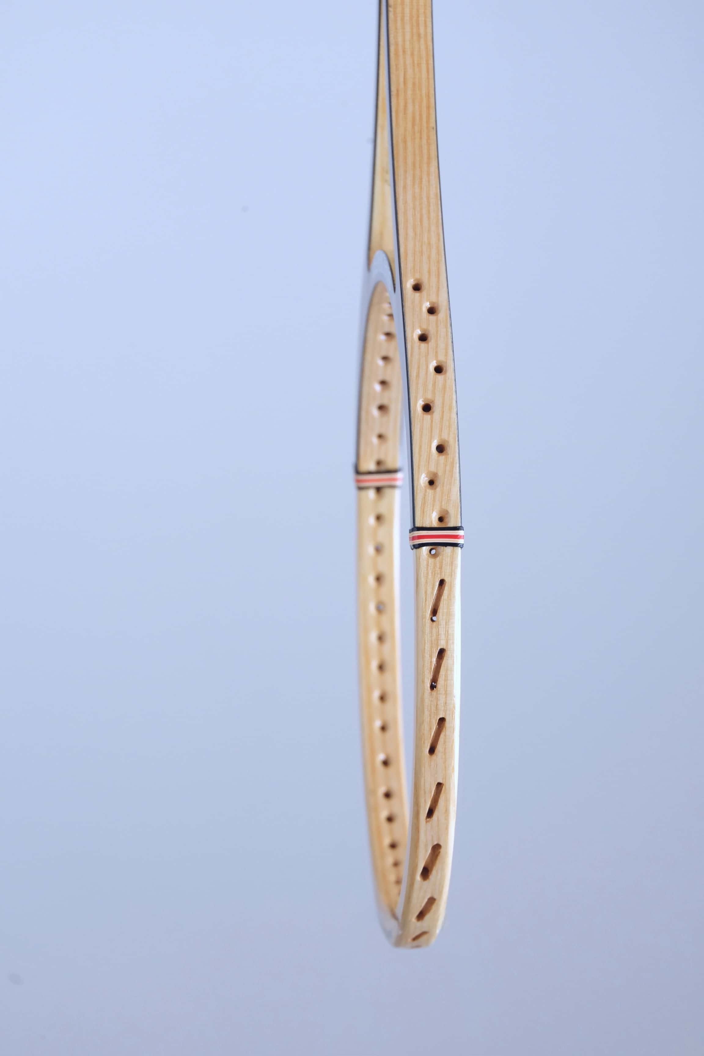 Profile close-up of the wood laminate frame and pre-drilled string holes of a vintage Snauwaert squash racket.