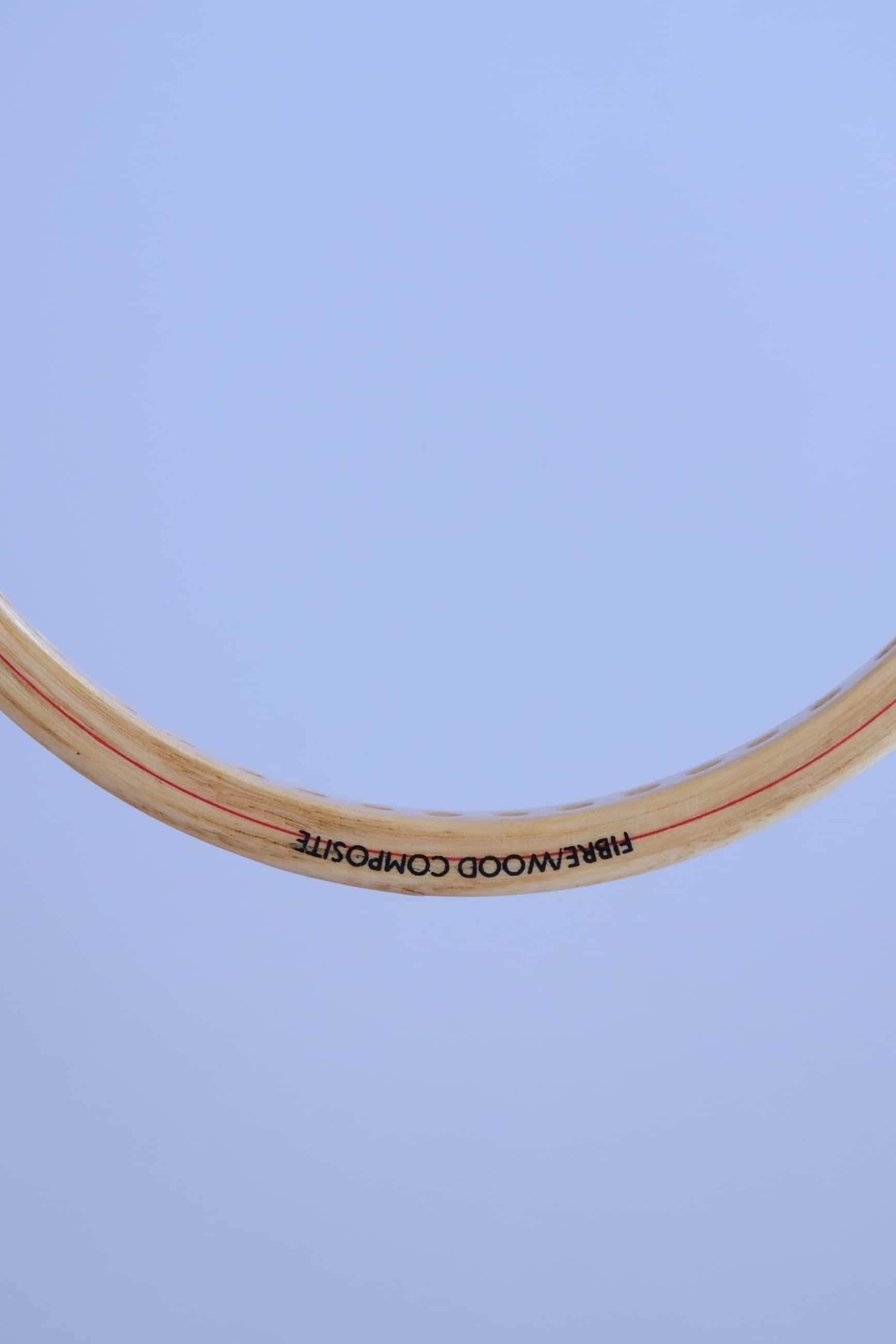 Close-up of the top curve of a vintage wood squash racket frame showing the text Fibre Wood Composite.