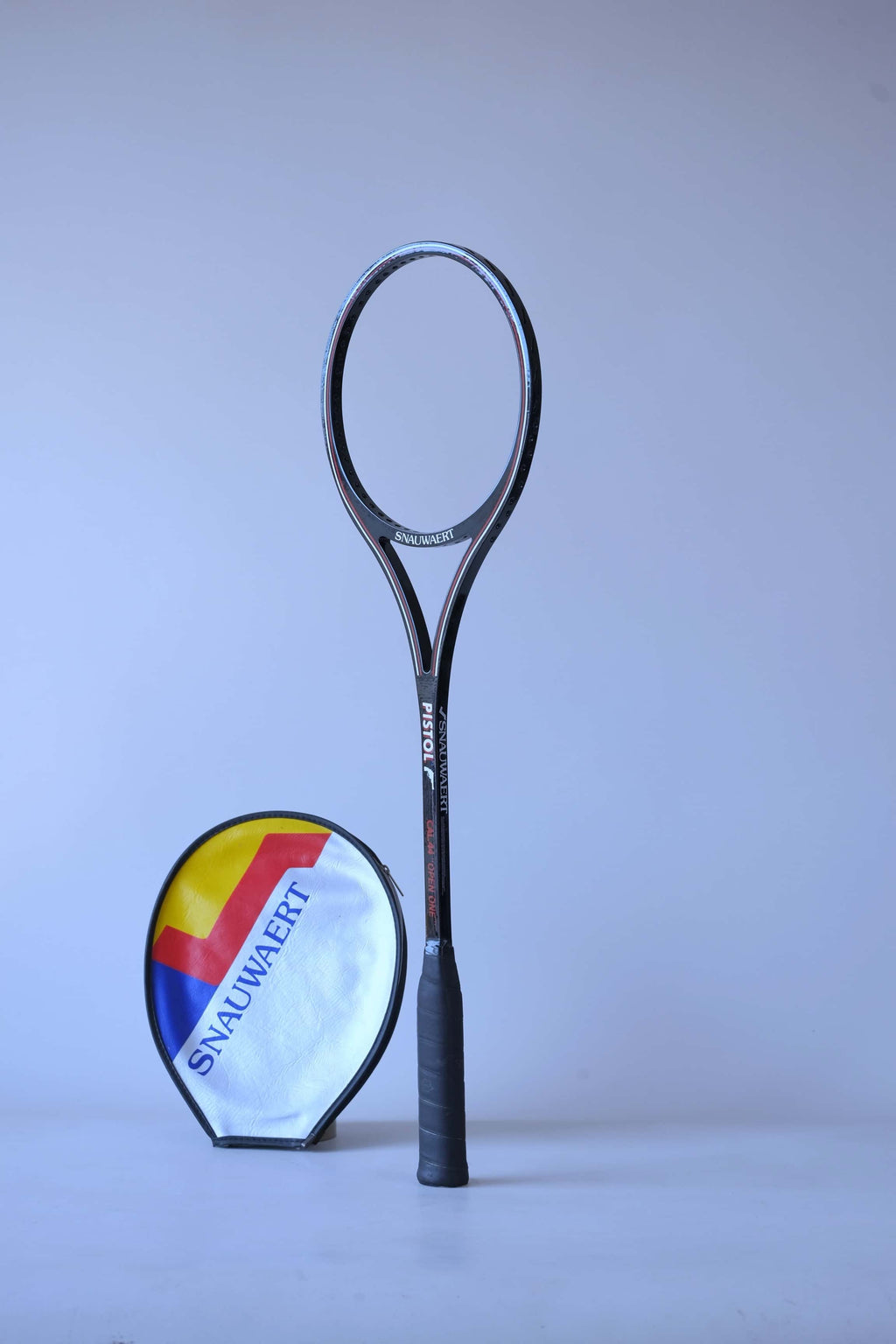 Angled view of an unstrung black vintage Snauwaert Pistol squash racket standing next to its vinyl cover.