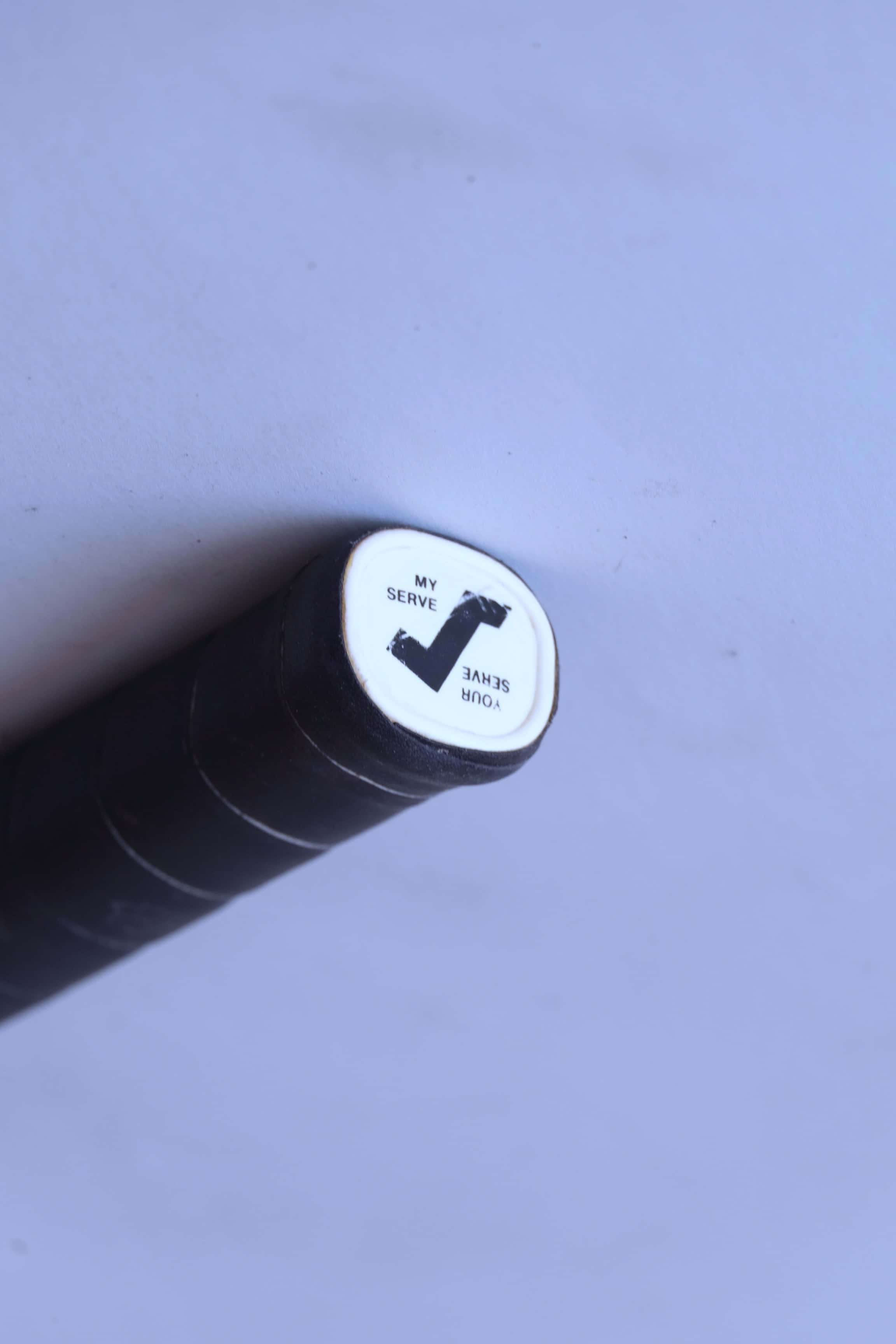 Close-up of the white plastic butt cap on a vintage squash racket handle featuring a black Snauwaert logo and the words Your Serve and My Serve.