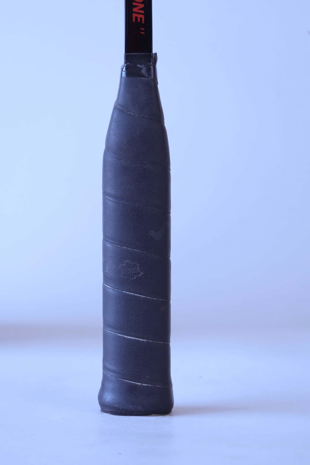 Close-up view of the original black textured leather wrap grip on a vintage squash racket handle.